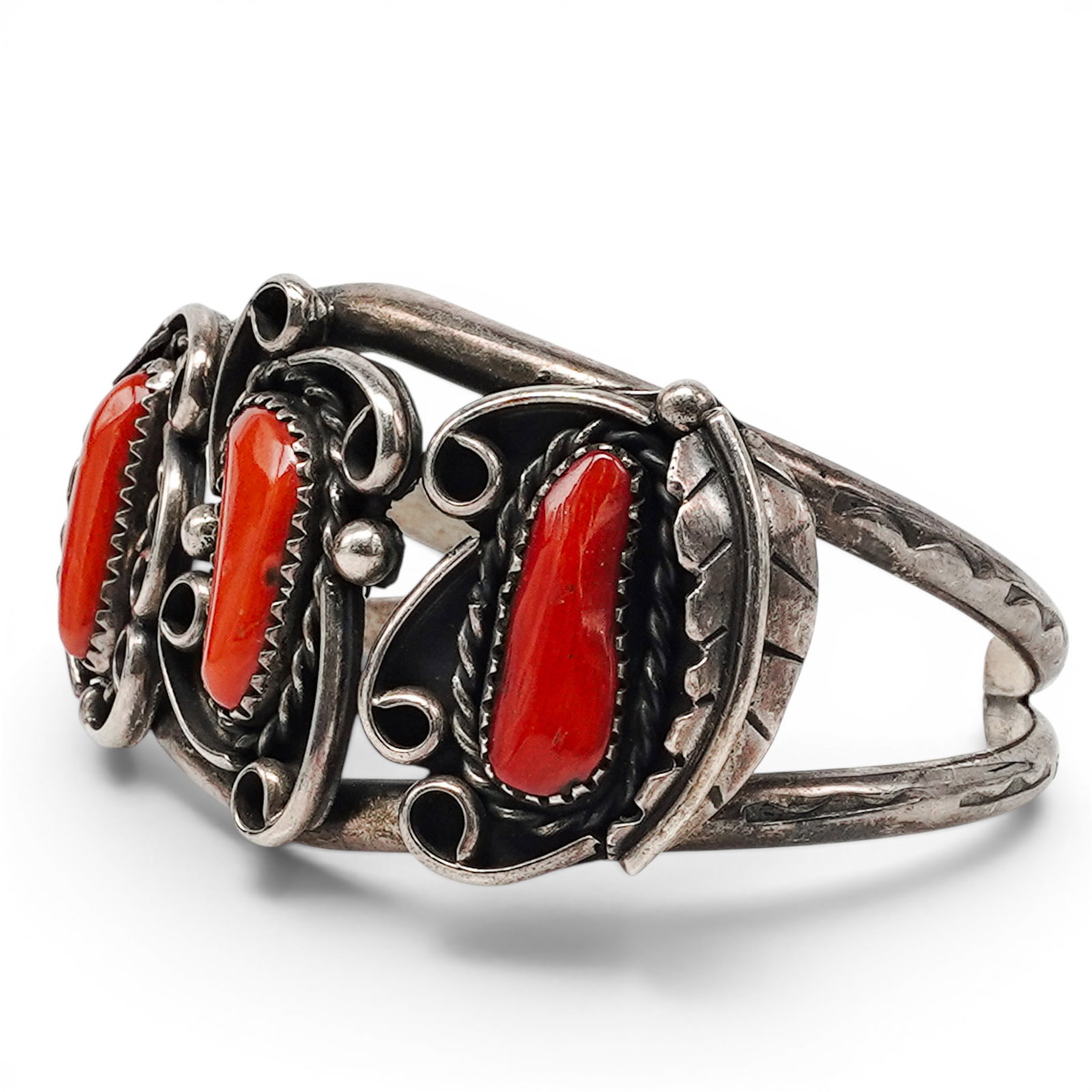 A Navajo Silver And Coral Three Stone Cuff Bracelet: A Navajo Silver And Coral Three Stone Cuff Bracelet Late 20th century Unmarked. Tested sterling silver. A cuff bracelet with three elongated coral cabochons in serrated bezels, joined by open scrollwo