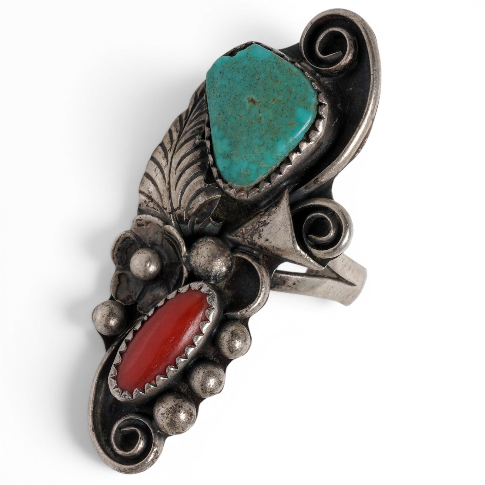 A Phil Chapo Navajo Sterling Silver, Turquoise, And Coral Scrollwork Ring: A Phil Chapo Navajo Sterling Silver, Turquoise, And Coral Scrollwork Ring Late 20th century Stamped: Phil Chapo. Tested sterling silver. A vertical ring set with turquoise and coral cabochons in serra