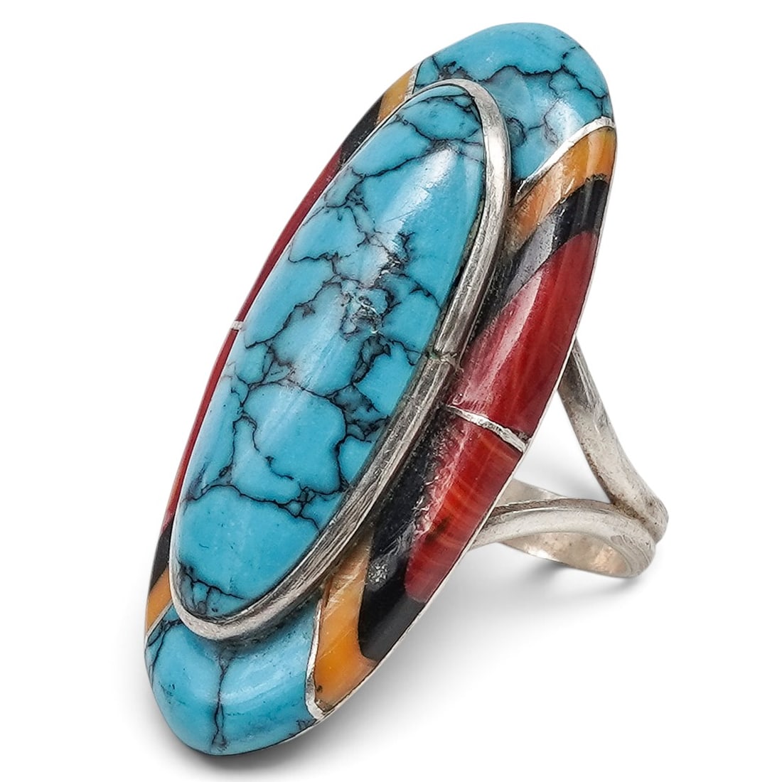 An Irene Platero Navajo Sterling Silver And Multistone Inlay Ring: An Irene Platero Navajo sterling silver and multistone inlay ring Late 20th Century Stamped: I.P. / Sterling. A ring with an elongated oval turquoise cabochon framed by channel-set multistone inlay of