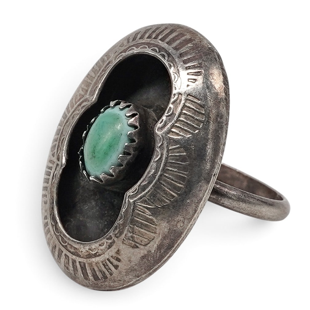 A Navajo Sterling Silver And Turquoise Shadowbox Ring: A Navajo sterling silver and turquoise shadowbox ring Late 20th century Unmarked. A domed ring centering an oval turquoise cabochon in a shadowbox setting with engraved geometric decoration to the sur