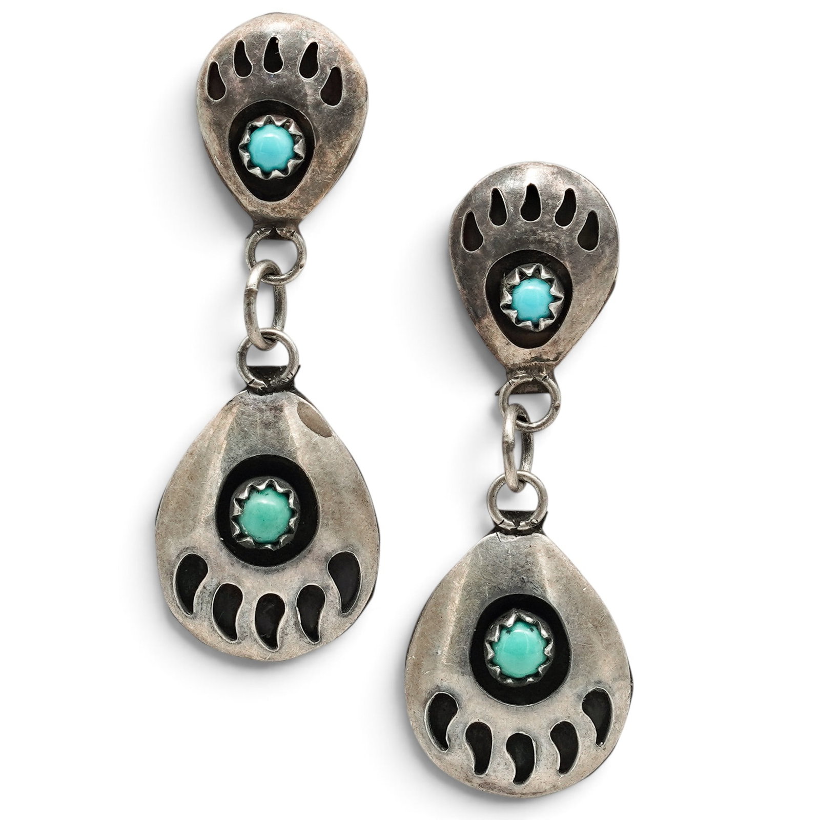 A Pair Of Navajo Sterling Silver And Turquoise Bear Paw Earrings: A pair of Navajo sterling silver and turquoise bear paw earrings Late 20th century Unmarked Tests for sterling. Each post earring suspends a pierced bear paw-form drop set with a small round turquoise