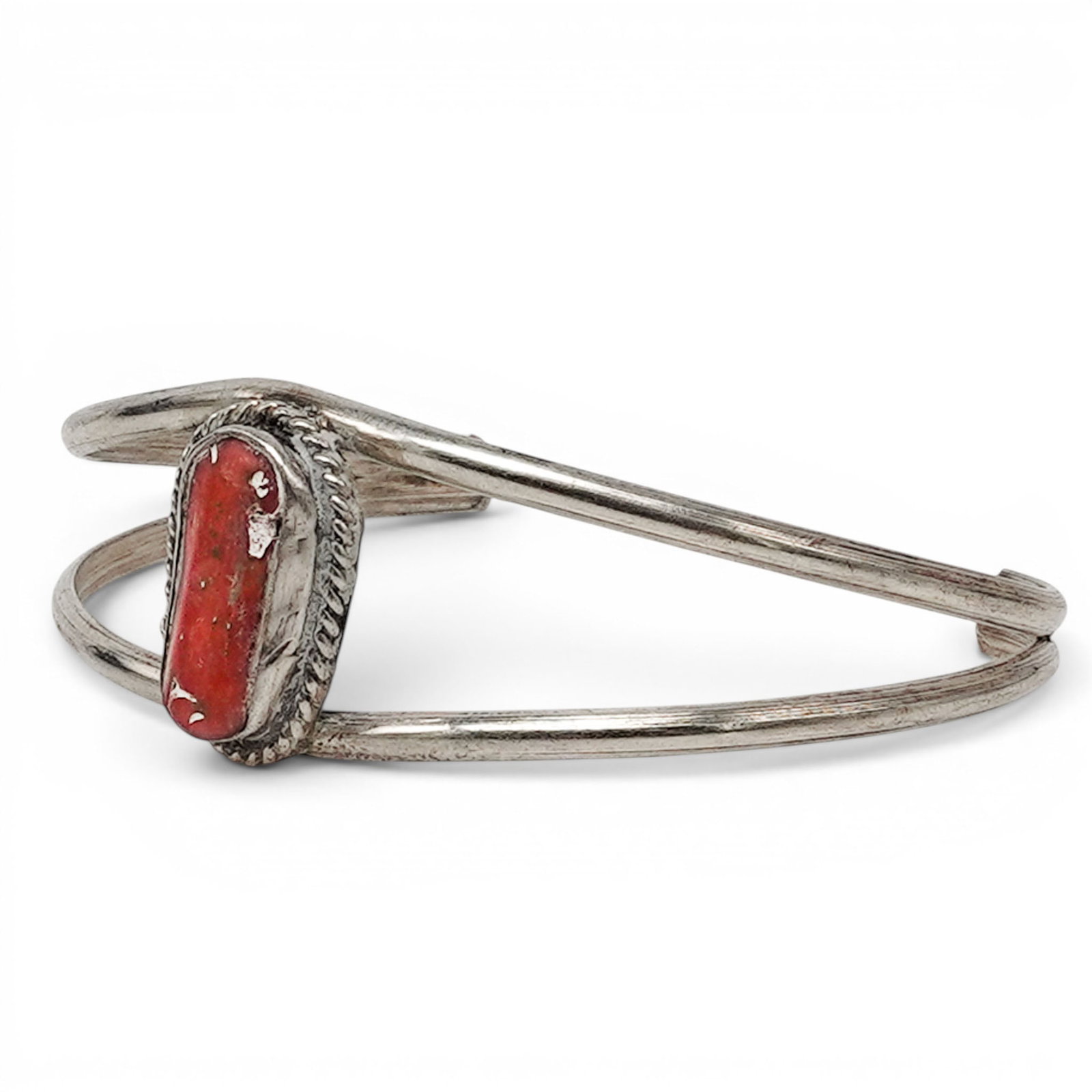 A Navajo Sterling Silver And Coral Single Stone Cuff Bracelet: A Navajo sterling silver and coral single stone cuff bracelet Late 20th century Unmarked. Tested sterling silver. A delicate cuff bracelet with a rectangular coral cabochon in a serrated bezel, accent