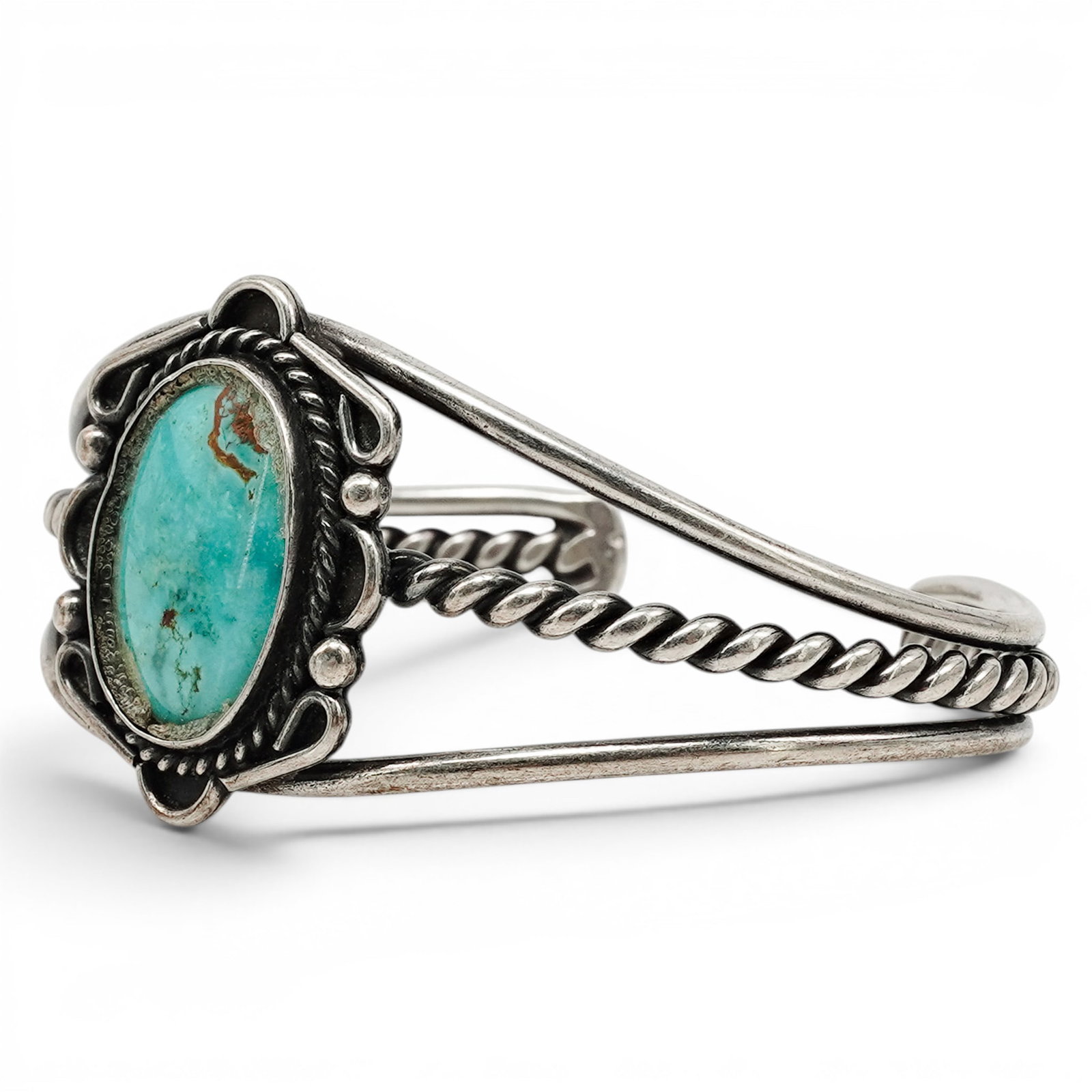 A Navajo Sterling Silver And Turquoise Scrollwork Cuff Bracelet: A Navajo sterling silver and turquoise scrollwork cuff bracelet Late 20th century Stamped: Sterling / Handmade. A cuff bracelet with a central round bezel set turquoise cabochon, accented by twisted w