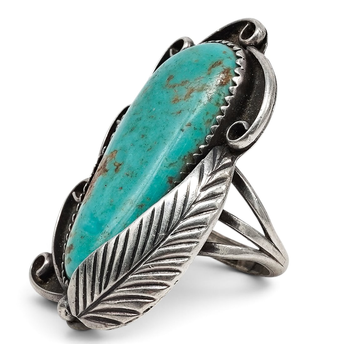 A Navajo Sterling Silver And Turquoise Scrollwork Ring: A Navajo sterling silver and turquoise scrollwork ring Late 20th century Unmarked. Tested sterling silver. An elongated ring set with a long oval turquoise cabochon in a serrated bezel, with open scro