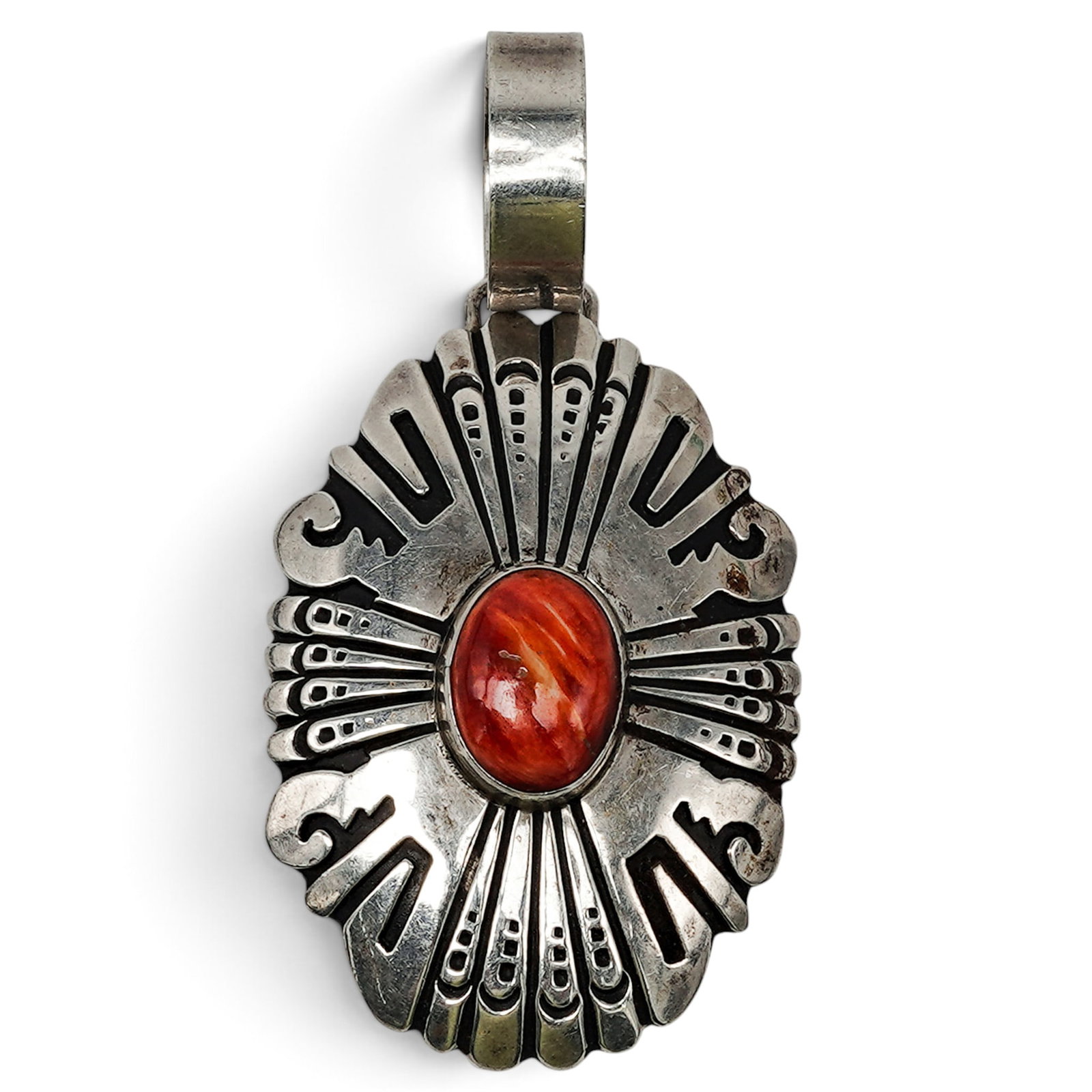 A Tommy Singer Navajo Sterling Silver And Coral Overlay Pendant: A Tommy Singer Navajo sterling silver and coral overlay pendant Late 20th century Stamped: T. Singer / Sterling An oval overlay pendant with radiating geometric motifs and a central oval coral cabocho