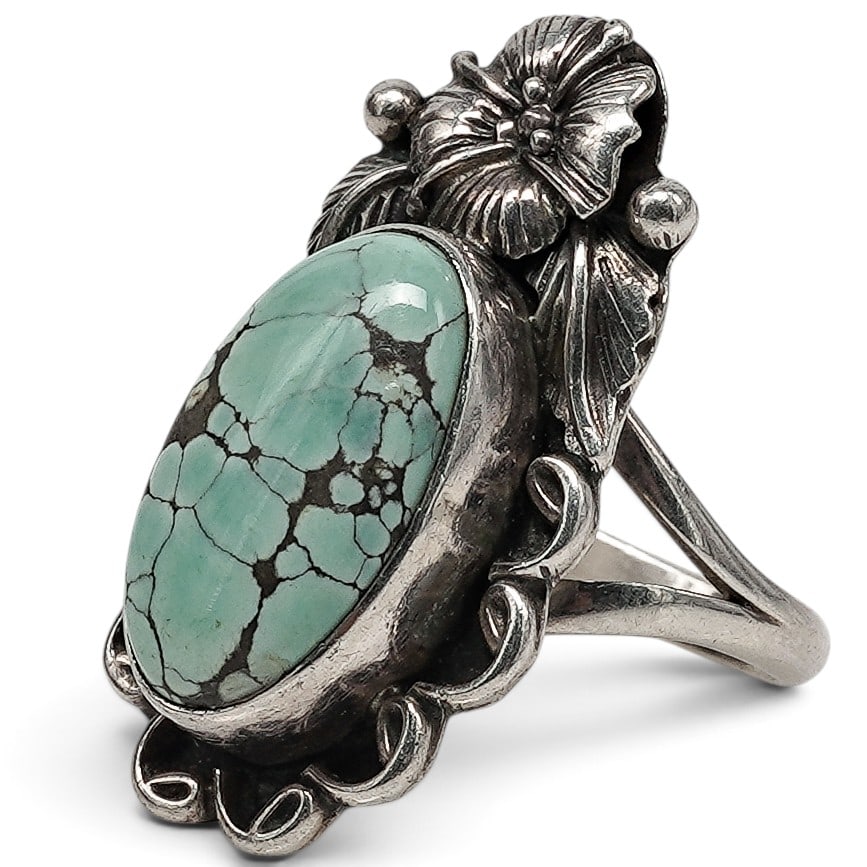 An Anthony Skeet Navajo Sterling Silver And Turquoise Floral Ring: An Anthony Skeet Navajo sterling silver and turquoise floral ring Late 20th century Stamped: A.S. / Sterling. A ring with an oval bezel-set turquoise cabochon framed by openwork scrollwork, applied fl