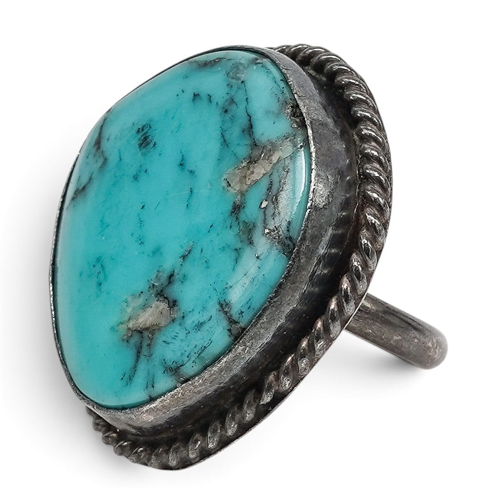 A Navajo Sterling Silver And Large Turquoise Ropework Ring: A Navajo sterling silver and large turquoise ropework ring Late 20th century Unmarked. Tested sterling silver. A ring set with a large oval turquoise cabochon with light matrix in a serrated bezel, fr