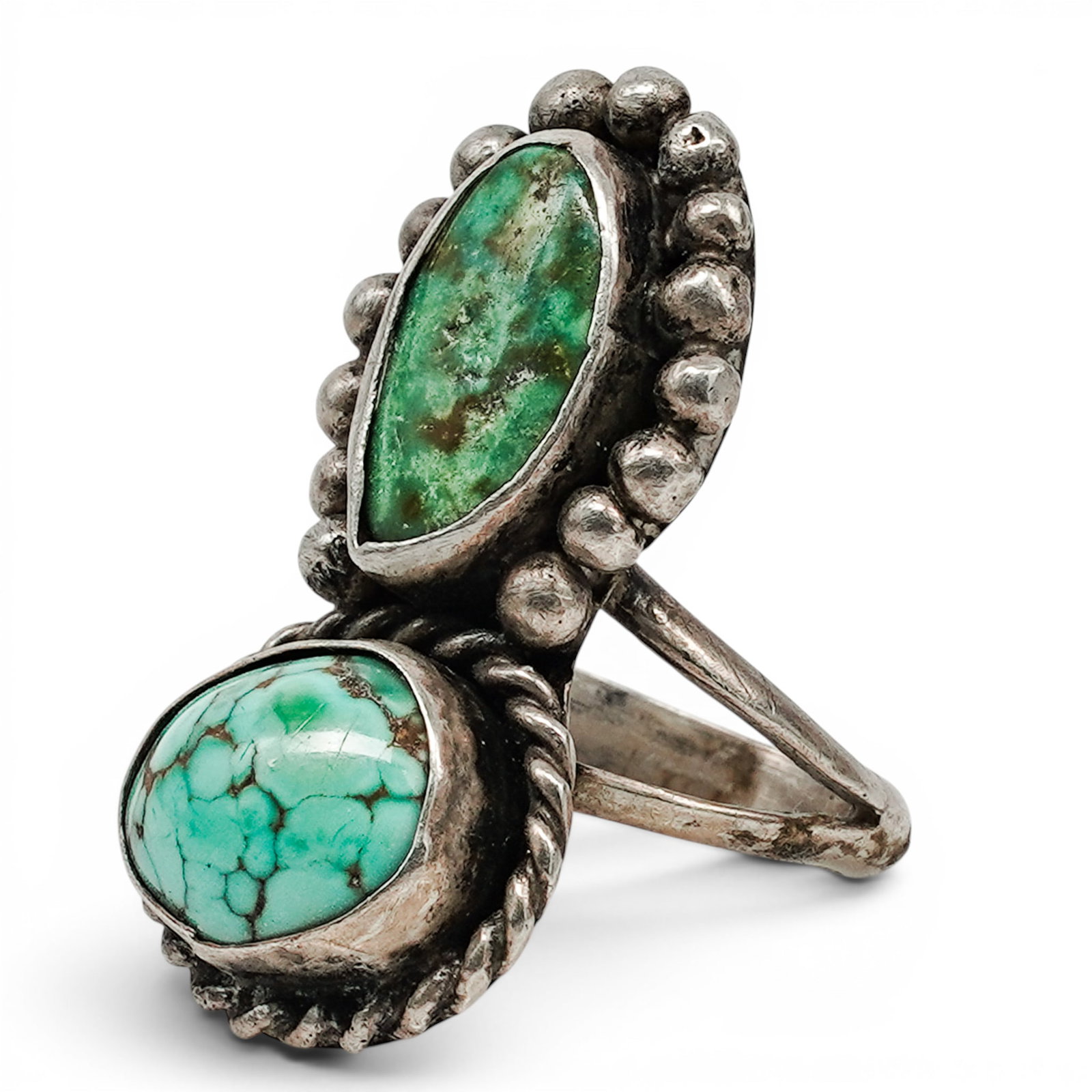 A Navajo Sterling Silver Double Turquoise Ring: A Navajo sterling silver double turquoise ring Late 20th century Unmarked. Tested sterling silver. A bypass-style ring set with two turquoise cabochons in bezel mounts, accented with applied silver be