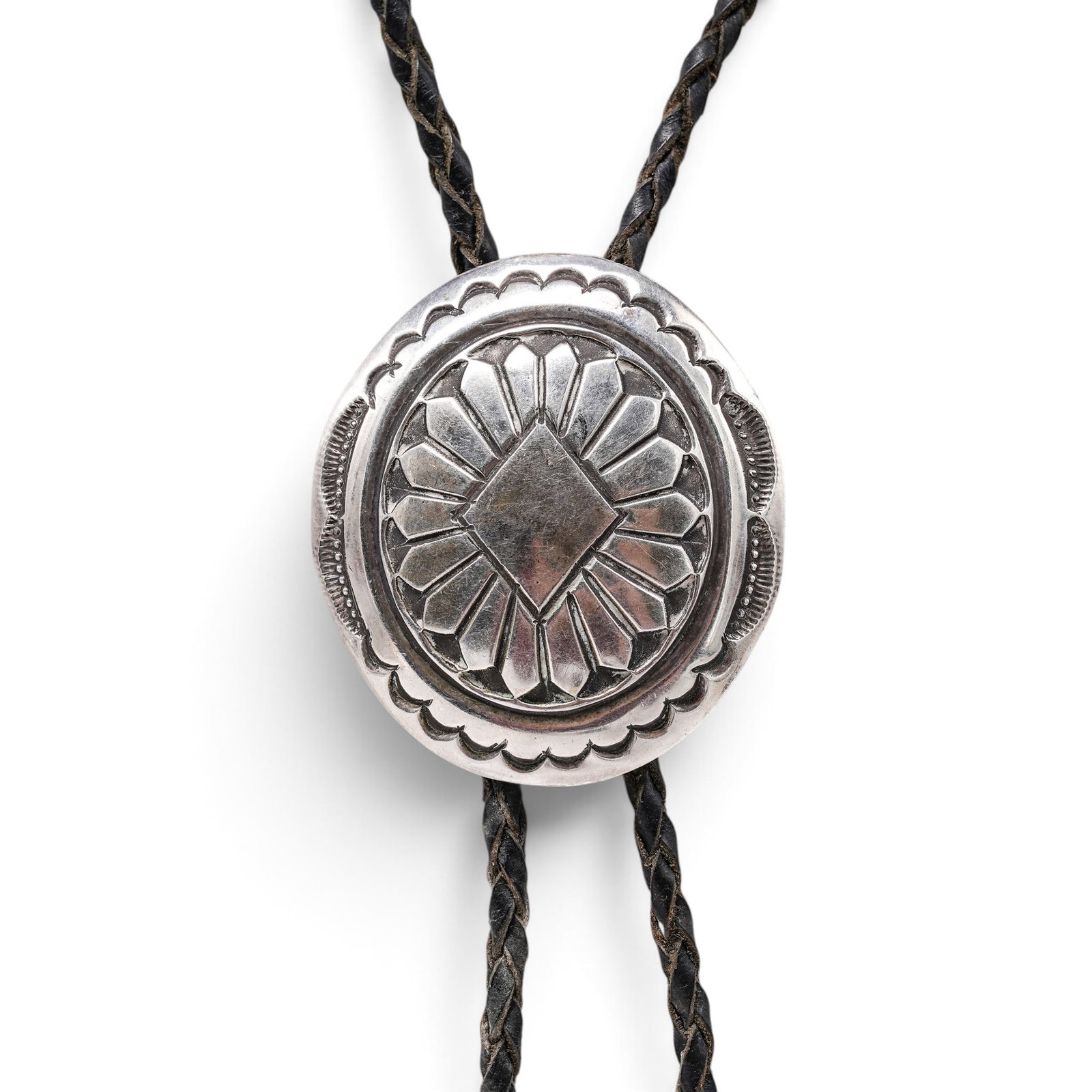 A Navajo Sterling Silver Stamped Concho Bolo Tie: A Navajo sterling silver stamped concho bolo tie Late 20th century Unmarked. Tested sterling silver. A bolo tie with a circular concho-form slide featuring radiating stampwork and geometric border dec
