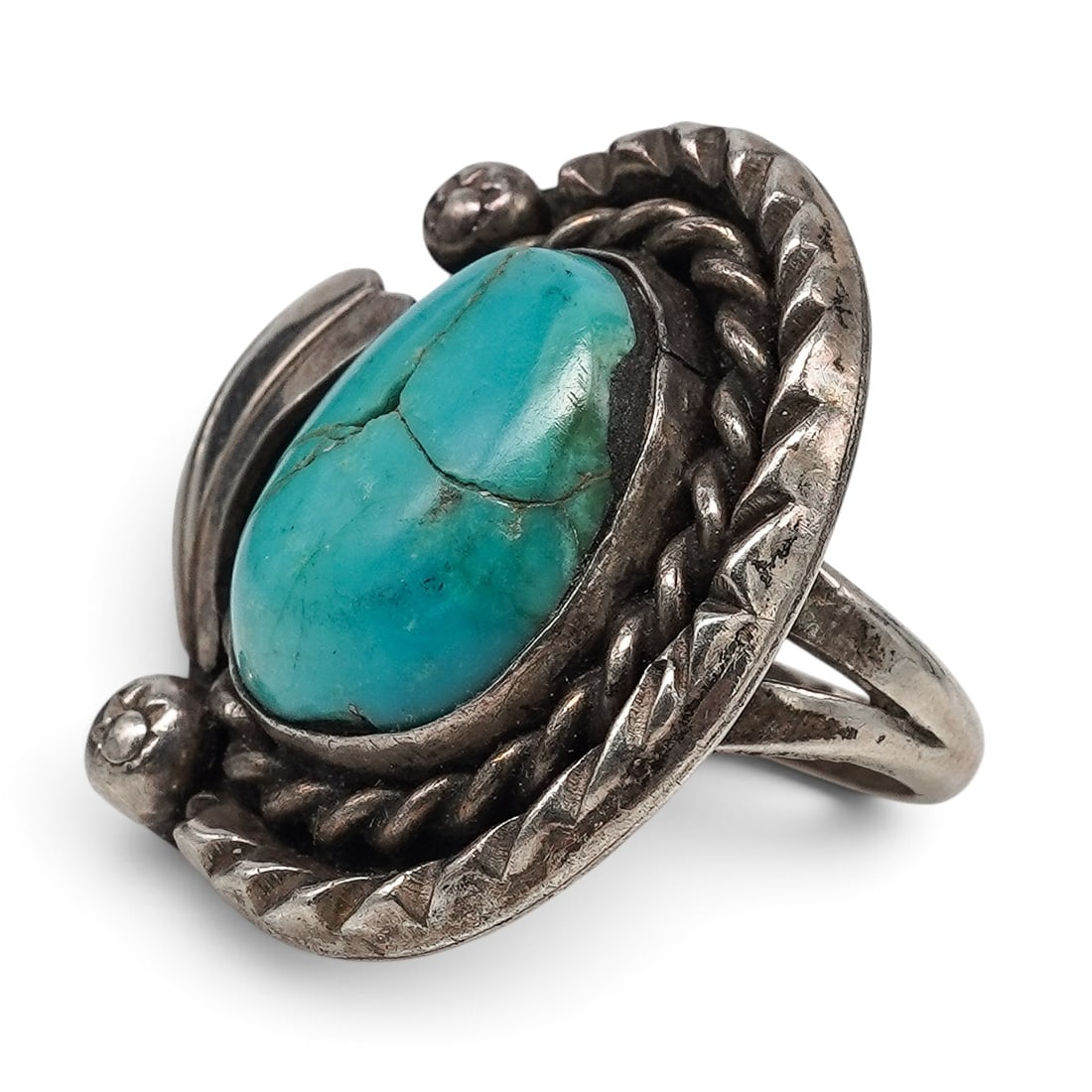 A Navajo Sterling Silver And Turquoise Ropework Motif Ring: A Navajo sterling silver and turquoise ropework motif ring Late 20th century Unmarked. Tested sterling silver. A ring set with an oval turquoise cabochon in a bezel setting, framed by horseshoe-form t