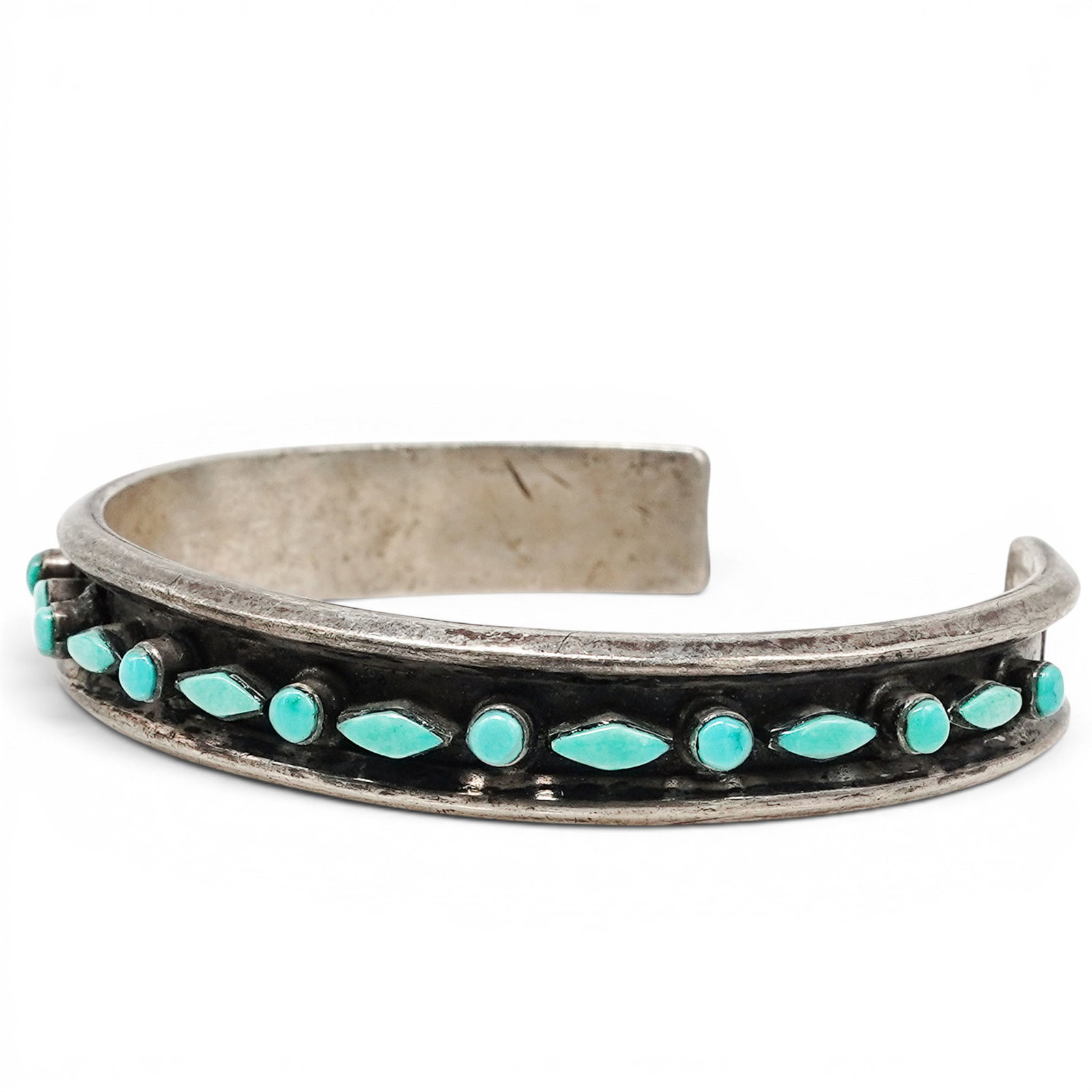 A Navajo Sterling Silver And Turquoise Row Cuff Bracelet: A Navajo sterling silver and turquoise row cuff bracelet Late 20th century Unmarked. Tested sterling silver. A narrow cuff bracelet with a graduated row of turquoise cabochons in bezel mounts, framed 
