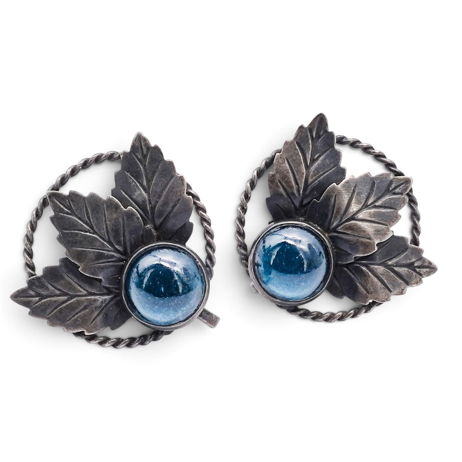 A Pair Of Navajo Sterling Silver And Blue Glass Leaf Clip-on Earrings: A pair of Navajo sterling silver and blue glass leaf clip-on earrings Late 20th century Stamped: Sterling. Clip earrings with round blue glass cabochons in bezel mounts, accented by applied leaf