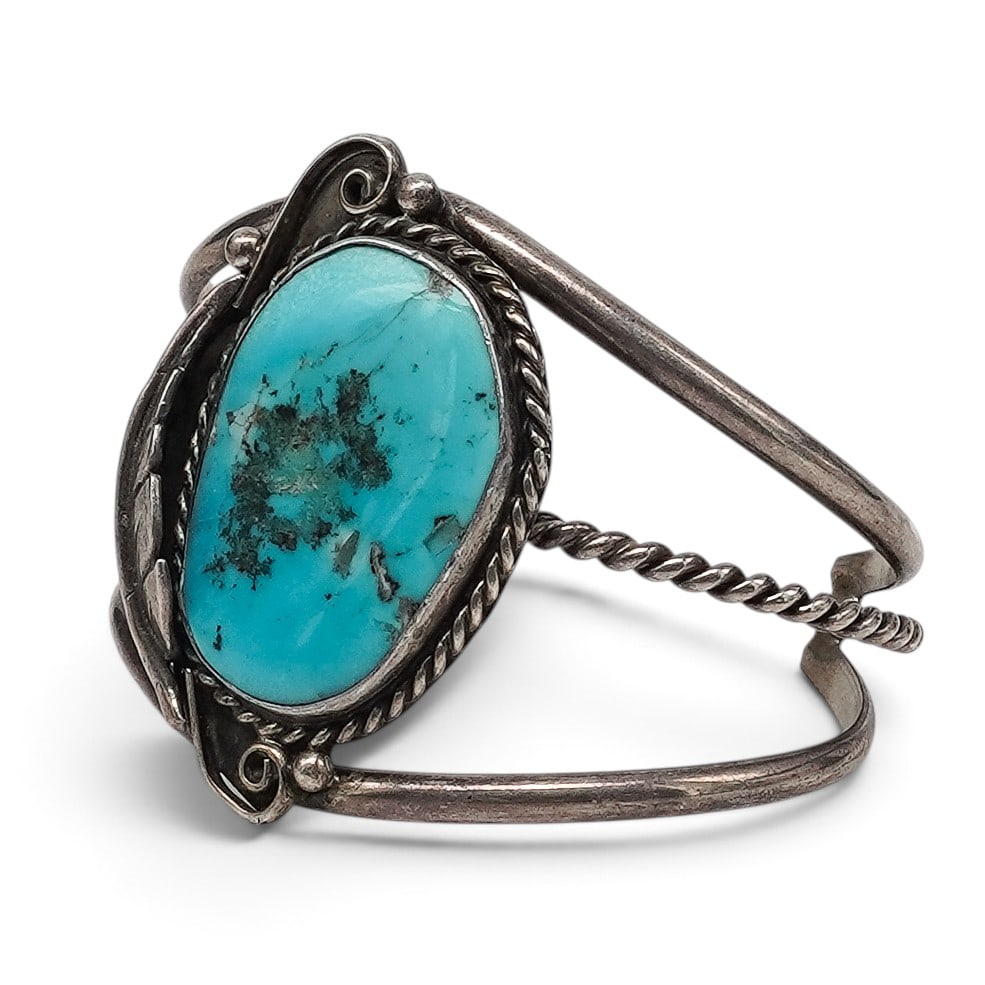 A Navajo Sterling Silver And Turquoise Cuff Bracelet: A Navajo sterling silver and turquoise cuff bracelet Late 20th Century Unmarked. Tested sterling silver. A three-wire cuff centered by a large oval bezel-set turquoise cabochon within a rope-twist bor