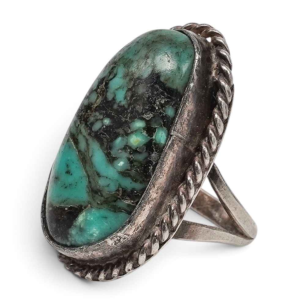 A Navajo Sterling Silver And Turquoise Ropework Ring: A Navajo sterling silver and turquoise ropework ring Late 20th century Unmarked. Tested sterling silver. A ring set with an elongated turquoise cabochon with dark matrix in a serrated bezel, surrounde