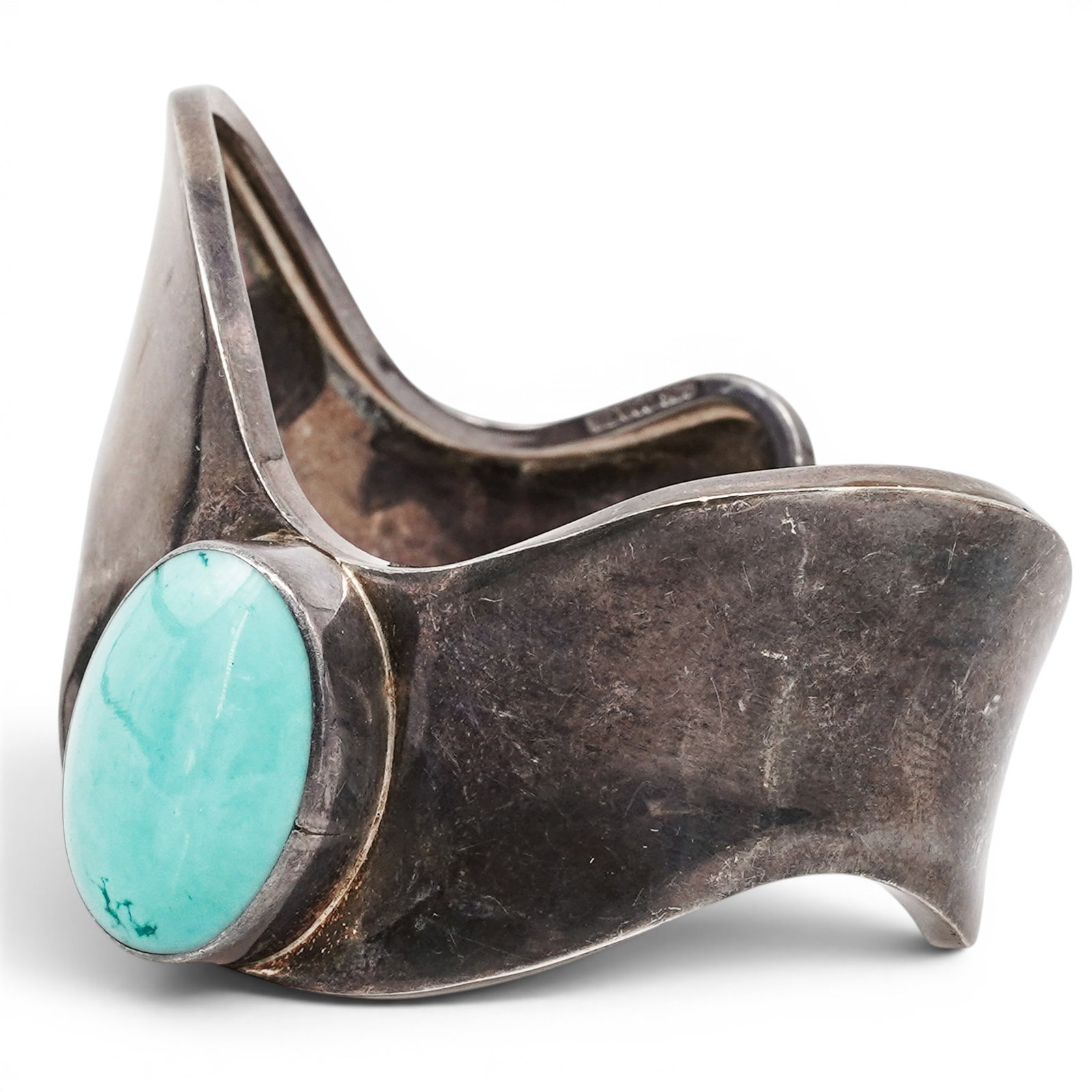 A Mexican Sterling Silver And Turquoise Modernist Cuff Bracelet: A Mexican sterling silver and turquoise modernist cuff bracelet Late 20th century Stamped: Mexico / .925 / TN-155. A sculptural silver cuff bracelet with a sweeping asymmetrical form, centered by an o