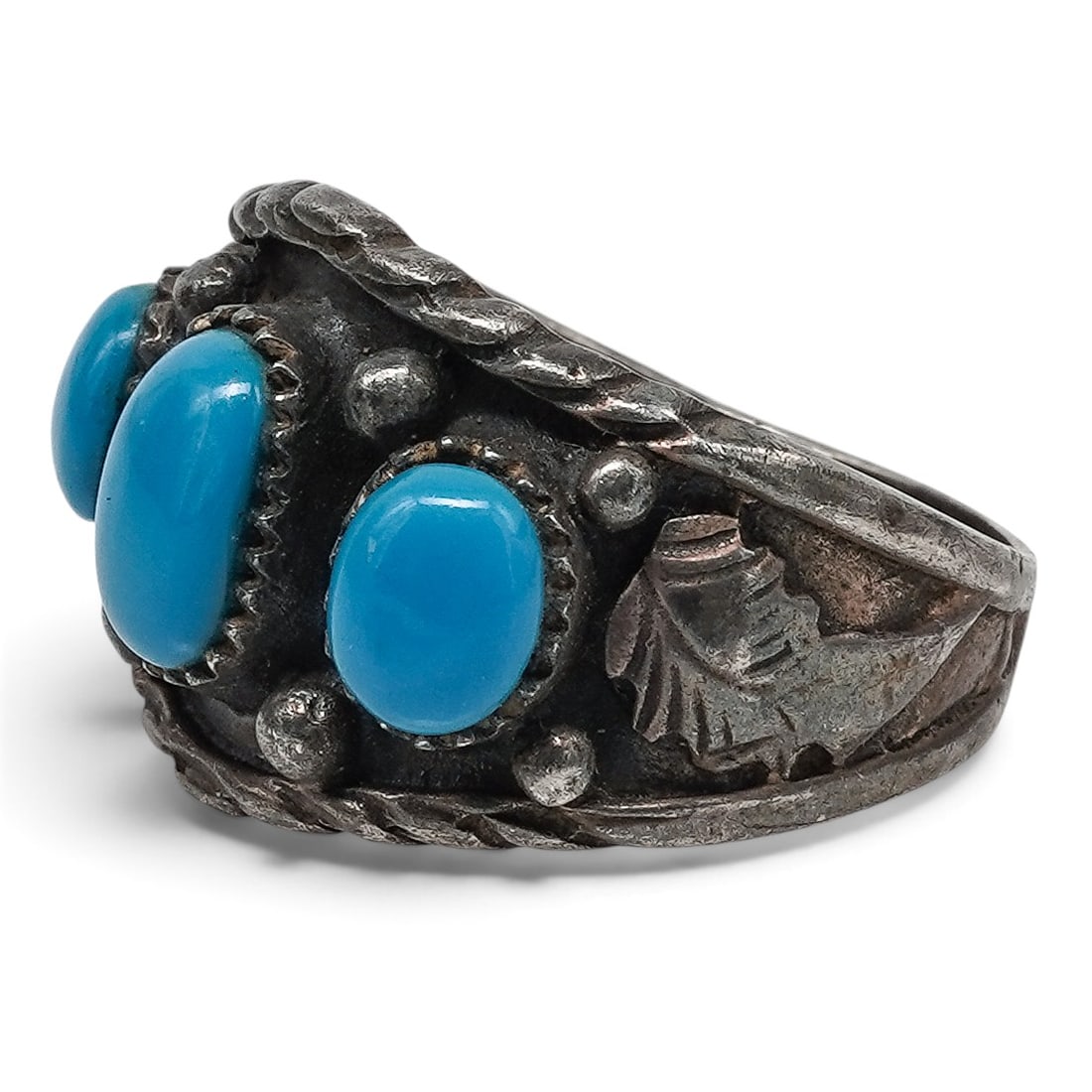 A Navajo Sterling Silver And Turquoise Three-stone Ring: A Navajo sterling silver and turquoise three-stone ring Late 20th century Stamped: 925. A wide silver band ring with three oval turquoise cabochons in serrated bezels, accented by applied silver beads