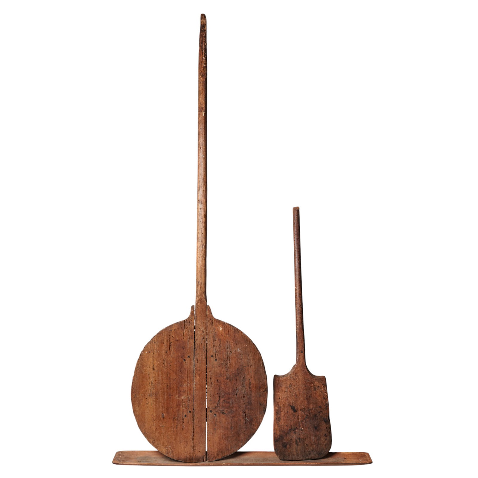 (3 pc) Antique French Bread Paddles w/ Plank: (3 pc) Antique French Bread Paddles w/ Plank 19th Cent, France Two antique wooden bakery paddles with weathered circular and rectangular blades resting against a rustic plank. L 75" x W 23" L 43 1/2"