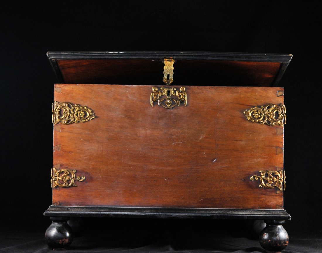 Antique pillow case/garment wood trunk: DESCRIPTION: Antique pillow case/garment wood trunk. Solid hard wood construction with dove tail joints. Gilt metal brackets, handles and latch with a foliate and putti motif. Sits a top four spherica