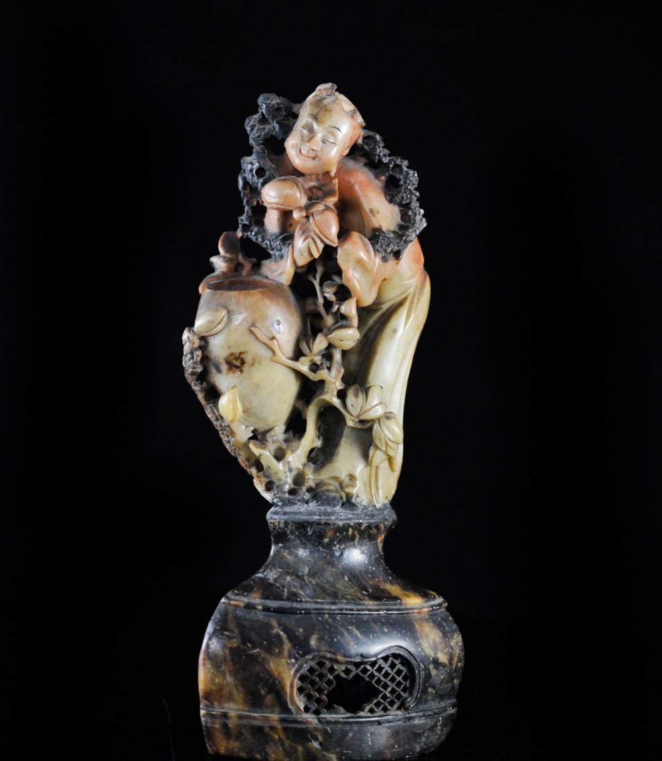 Large Antique Hand Carved Soapstone Figurine: DESCRIPTION: Large hand carved multi color soapstone smiling figurine in a floral motif, footed on soapstone base. Chipped on the base and top of figures head. CIRCA: 19/20th ct ORIGIN: China DIMENSIO