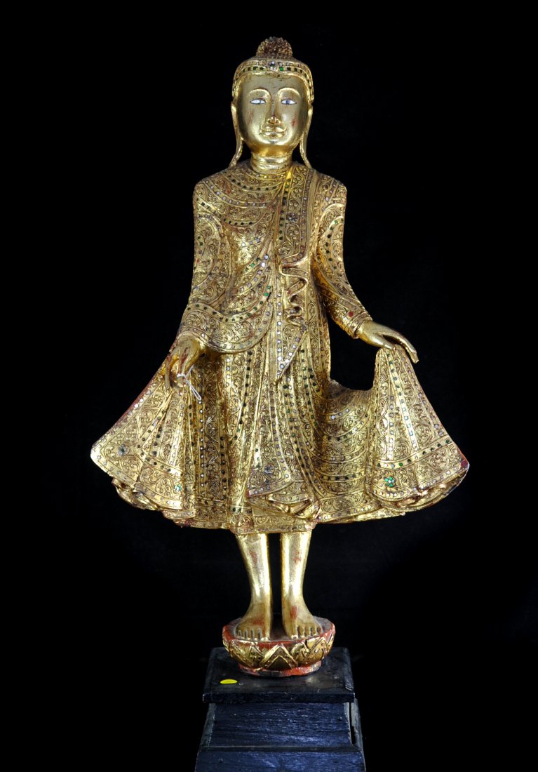 Wooden Hand Carved Thai Buddah: "DESCRIPTION: Thai gilt-wooden buddah standing on two feet with a serene face. Decorated with an elaborate crown and a long robe filled with embellished green jewlels slightly held open. Standing on a
