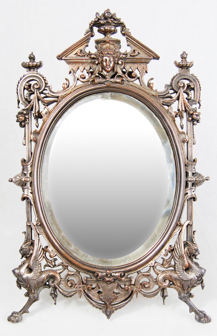 Antique Silver Bronze Footed Mirror: DESCRIPTION: A 19th century French ornate footed silver over bronze mirror. The two bottom legs are in the shape of winged lions standing on their hind legs.The Oval shaped mirror is crowned with the 