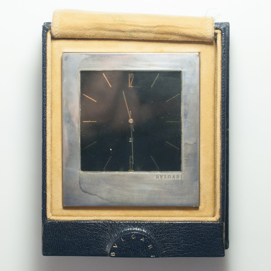 Bulgari Silver Desk Clock: DESCRIPTION: Sterling silver Bulgari clock with quartz movement, the square black dial with gold baton chapters and Arabic numerals, gold hands and a window for date, within a sterling silver case, co