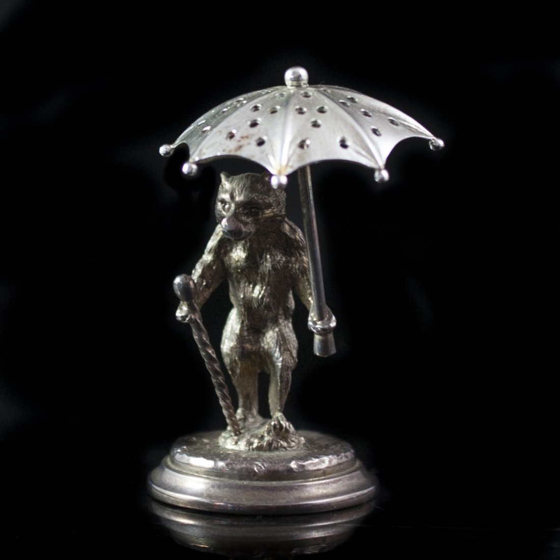 Christofle Silver Figurine: DESCRIPTION:Silver figurine by Christofle. Features a circus bear holding a spiraling cane and an umbrella with perforations. Rests on a circular base and marked: "Christofle" along with illegible hal