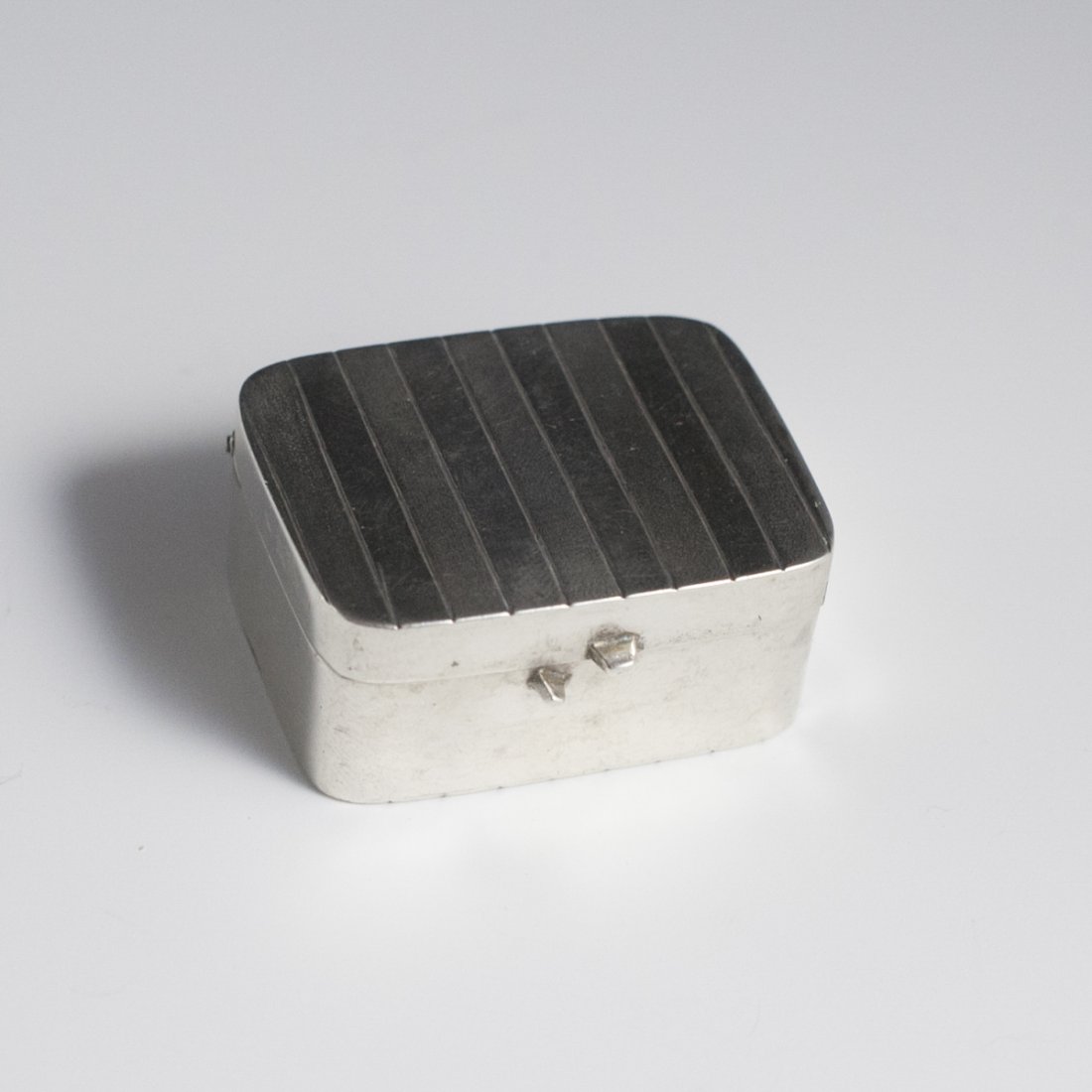 Sterling Pill Box: DESCRIPTION:Sterling pill box featuring a square shape with ridges along the lid and on the bottom. Marked:"925" CIRCA:20th Ct. ORIGIN:Unknown DIMENSIONS:H:0.5" L:1.75" Total Weight:33 grams CONDITION
