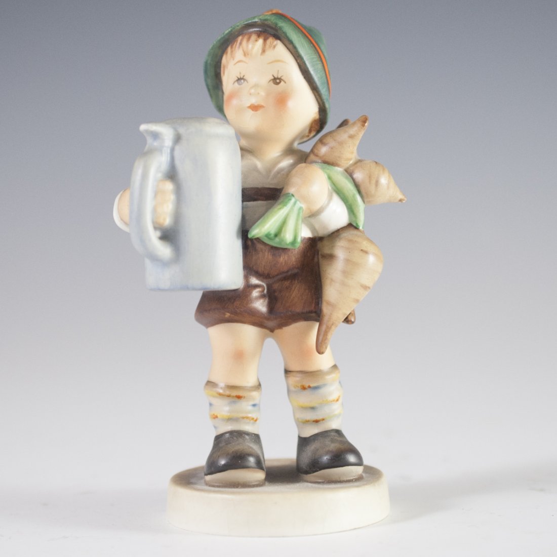 German Porcelain Figurine: DESCRIPTION: A German porcelain figurine of a young boy holding a cluster of carrots in one hand and a beer stein in the other, dressed in traditional German clothing. Finished with a matte polish and