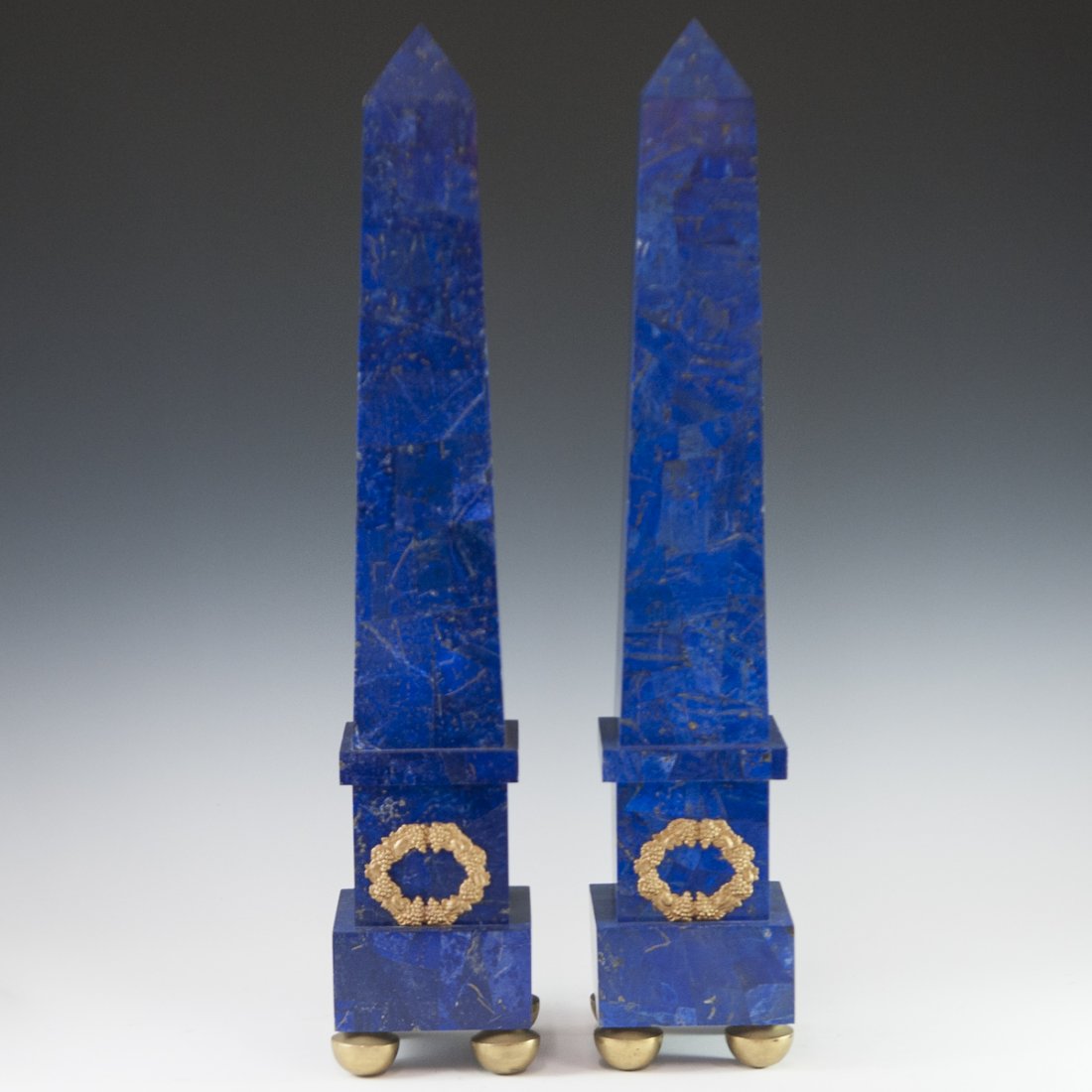 Pair of Lapis Lazuli & Dore Bronze Obelisks: DESCRIPTION: A pair of obelisks comprises of Lapis lazuli tiles and panels. Embellished with a dore bronze wreath of grape clusters. Finished with gilded bronze demi-spherical feet below the cubical b