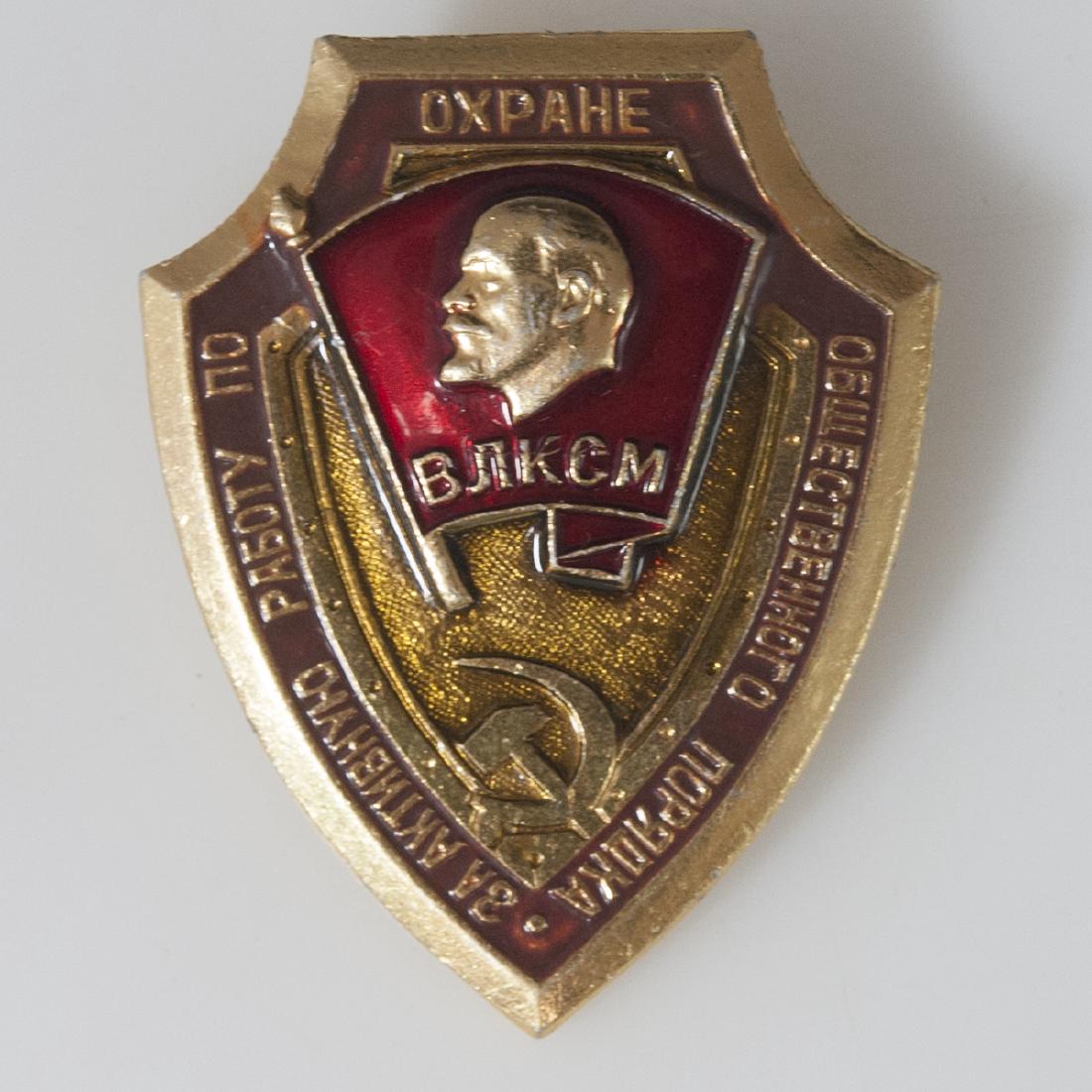 Soviet Icon of the Komsomol Pin: DESCRIPTION: A Soviet Icon of the Komsomol pin. Features the motif of a gilded shield, centered by a profile of Stalin enveloepd in a red enameled flag. Finished with Russian characters, CIRCA: 20th C