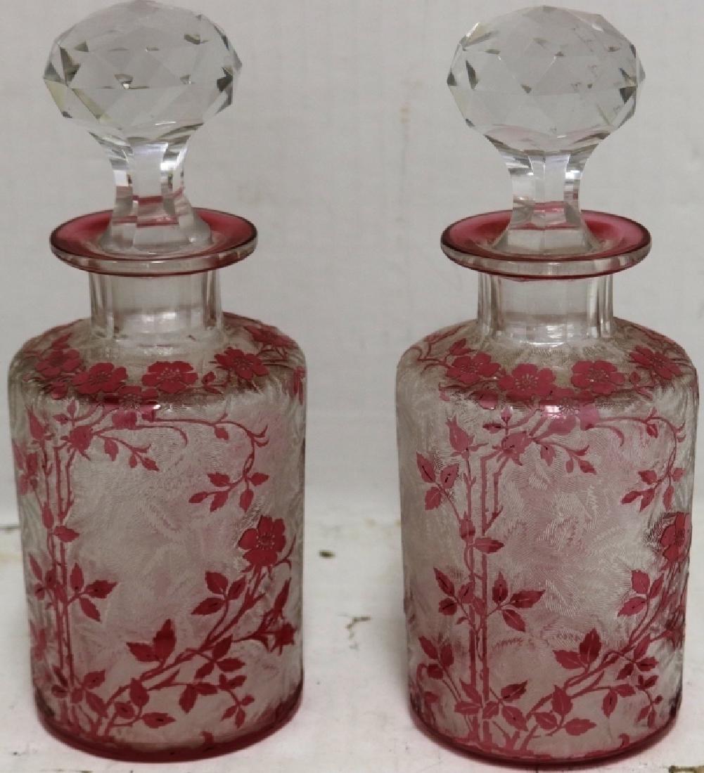 PAIR OF EARLY 20TH C FRENCH OVERLAY COLOGNE: BOTTLES BY BACCARAT. ENGRAVED FORM DESIGN WITH CRANBERRY FLORAL AND VINE OVERLAY. FACETED STOPPERS. 8" HIGH.