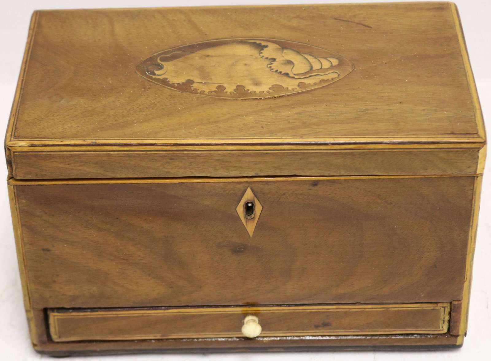 EARLY 19TH CENTURY INLAID MAHOGANY TEA CADDY WITH: DRAWER. OVAL INLAID SHELL ON TOP. DOUBLE COMPARTMENT INTERIOR AND DRAWER AT BOTTOM. POSSIBLY MISSING VENEER TO VERY BOTTOM EDGES. SHOWS REFINISHING. 6" HIGH, 9" WIDE, 5" DEEP.