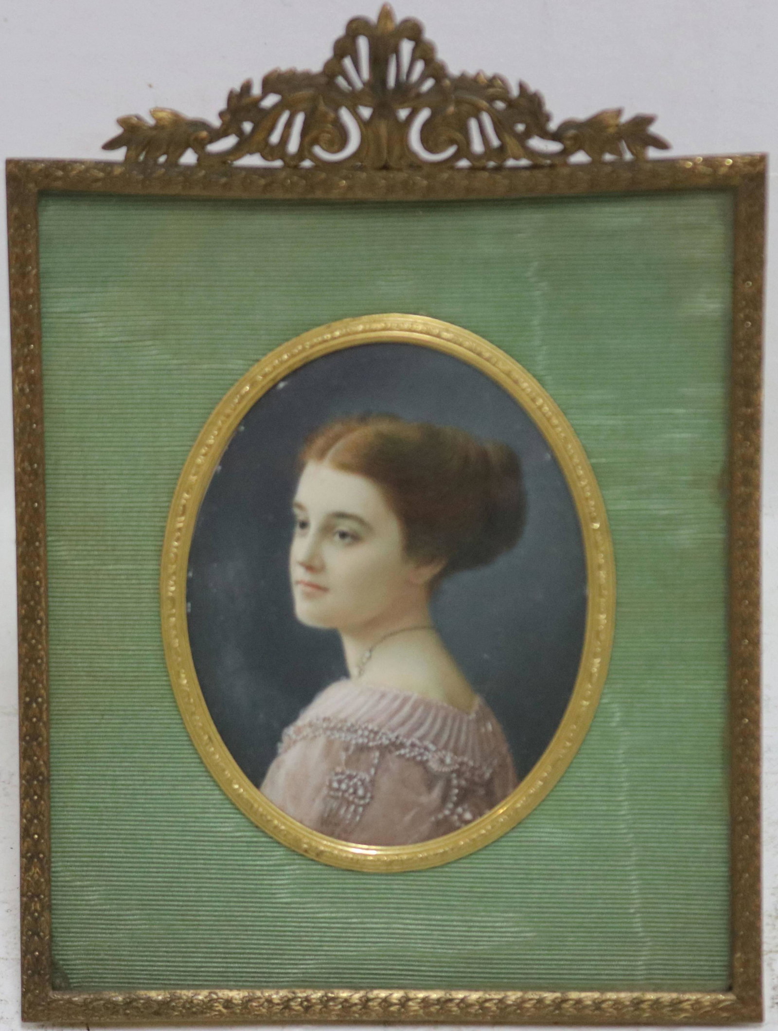 CA. 1910 FRAMED PORTRAIT MINIATURE PAINTING OF AN: ATTRACTIVE YOUNG LADY WEARING A PINK SILK AND BEADED EVENING GOWN. IN AN ENGRAVED BRASS FRAME. FRAME IS SIGNED "THE H. LIEBER COMPANY, INDIANAPOLIS". OVAL. SIGHT SIZE 3 1/2" X 2 3/4", OVERALL 6 1/2" X