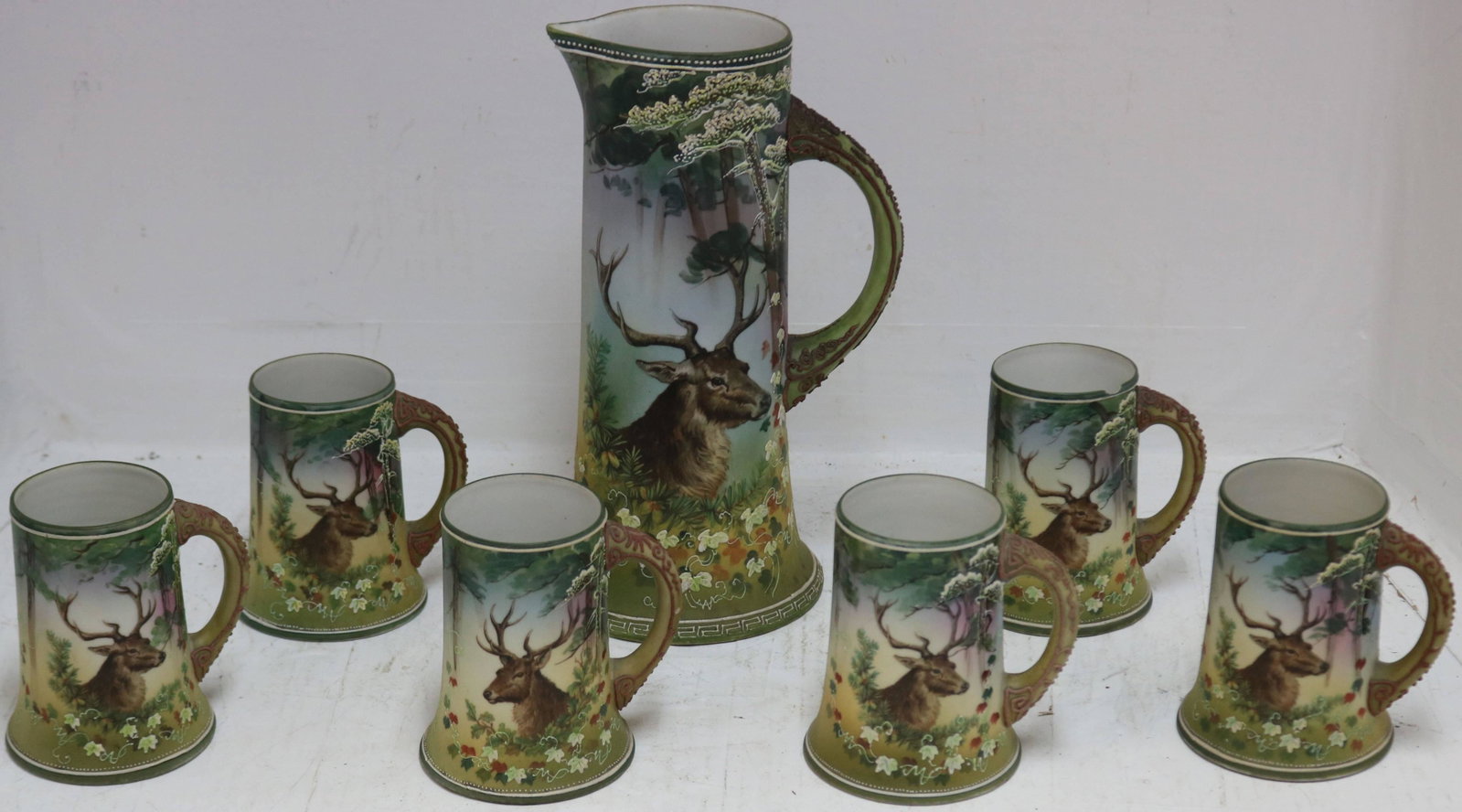 SEVEN PIECE NIPPON CIDER SET WITH 11" TANKARD: PITCHER AND SIX 4 3/4" HANDLED MUGS. HAND PAINTED, WITH STAG DESIGN. ONE MUG HAS A CHIP WITH HAIRLINE.