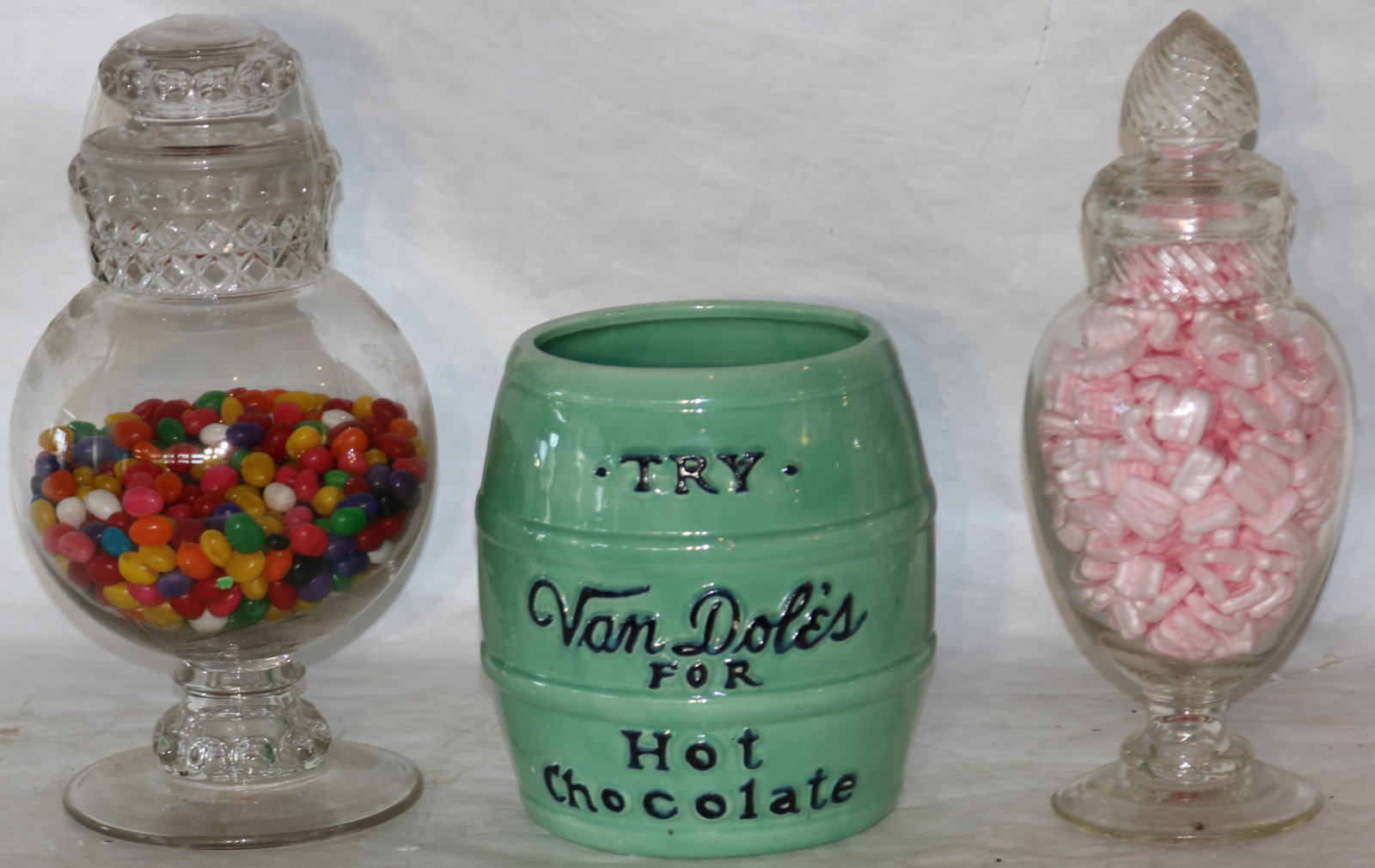 LOT OF 3 20TH CENTURY COUNTRY STORE DISPLAY JARS.: TO INCLUDE: 2 FOOTED GLASS CANDY JARS WITH LIDS, ONE 15" HIGH WITH FLATTENED SAW-TOOTH DESIGN (CHIP TO RIM), THE OTHER 15 1/2" HIGH WITH SWIRL DESIGN. ALONG WITH A CERAMIC ADVERTISING BARREL "TRY VAN 