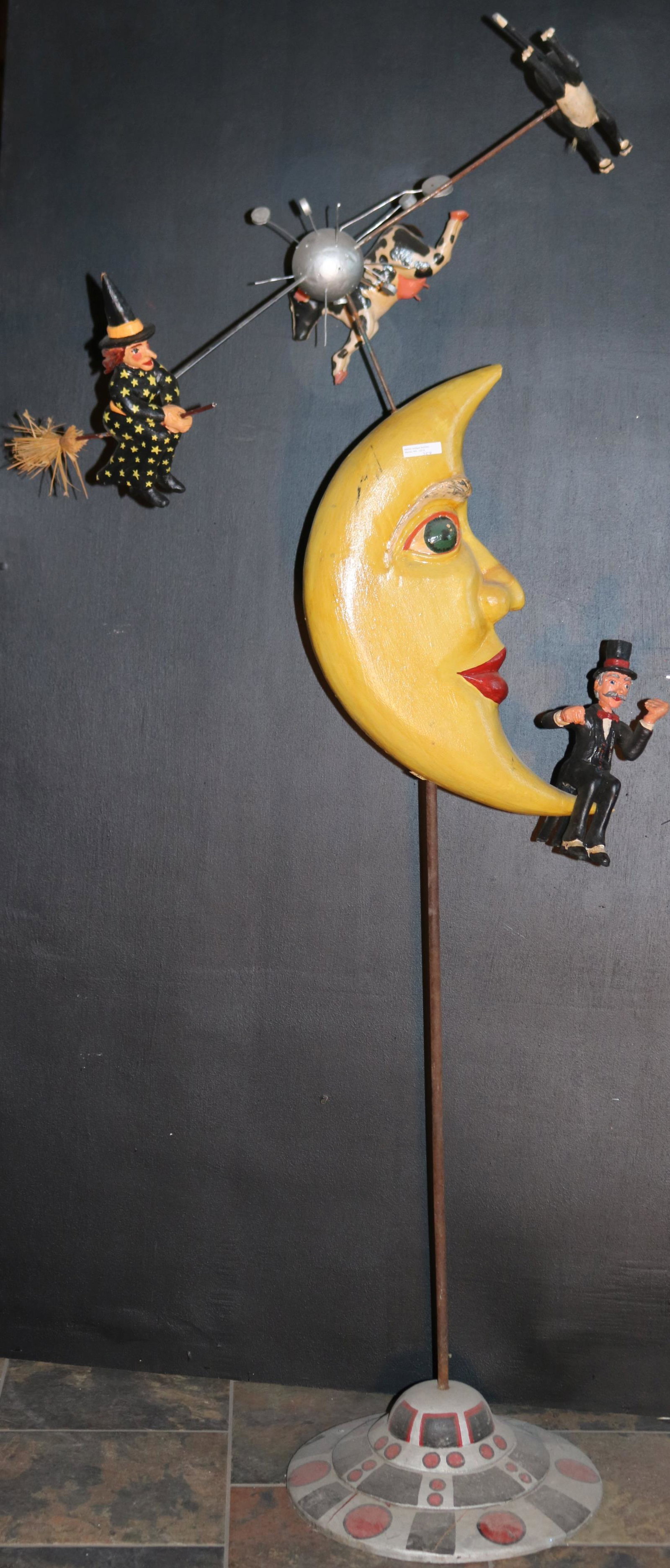 20TH CENTURY NURSERY RHYME FOLK ART SCULPTURE,: DEPICTING CAT, COW, WITCH, AND FIDDLER ORBITING THE MOON. BASE IS SHAPED AND PAINTED LIKE A UFO SPACESHIP. FIDDLER IS MISSING HIS FIDDLE. SMALL CHIP AT THE UPPER POINT OF THE MOON. APPROX. 64" HIGH, 2