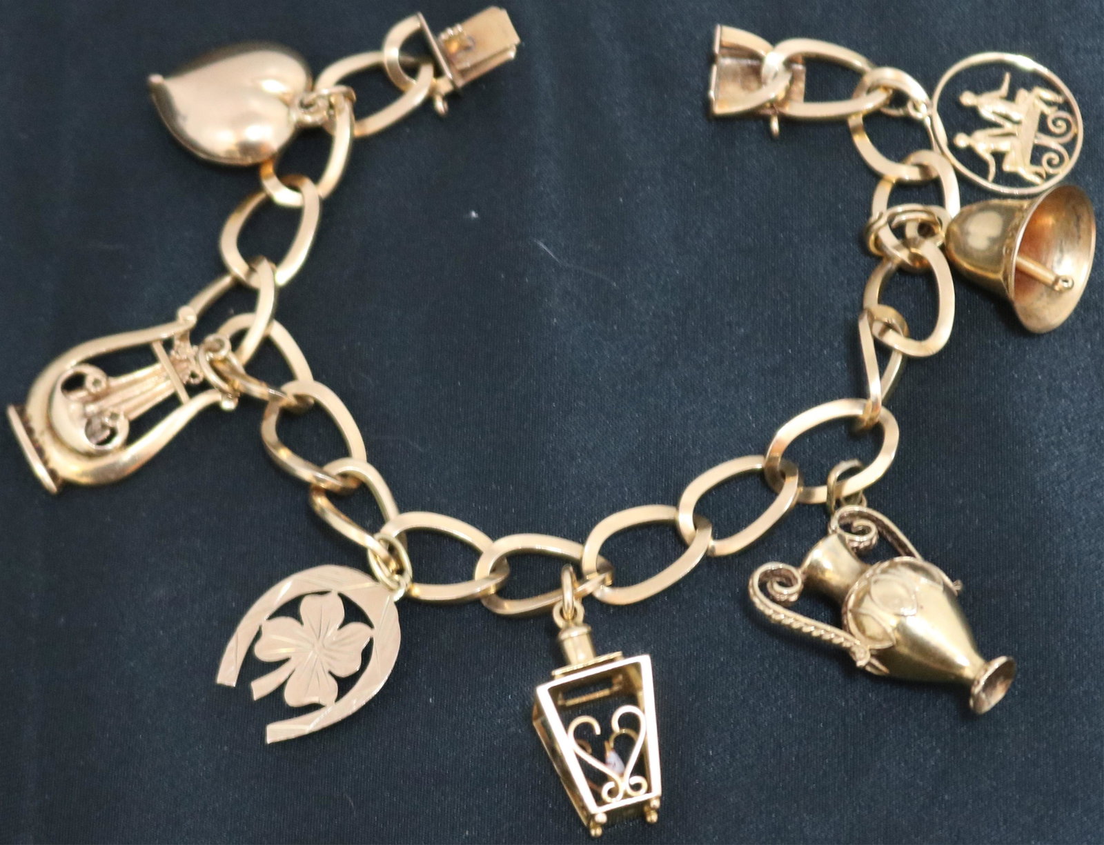 18KT YELLOW GOLD CHARM BRACELET WITH 7 CHARMS. 4: CHARMS AND 10KT (VASE, LANTERN, BARREL, PEOPLE), 3 CHARMS ARE 14KT (HEART, HORSESHOW WITH CLOVER, VASE). 7 1/2" LONG, 23.7 DWT.