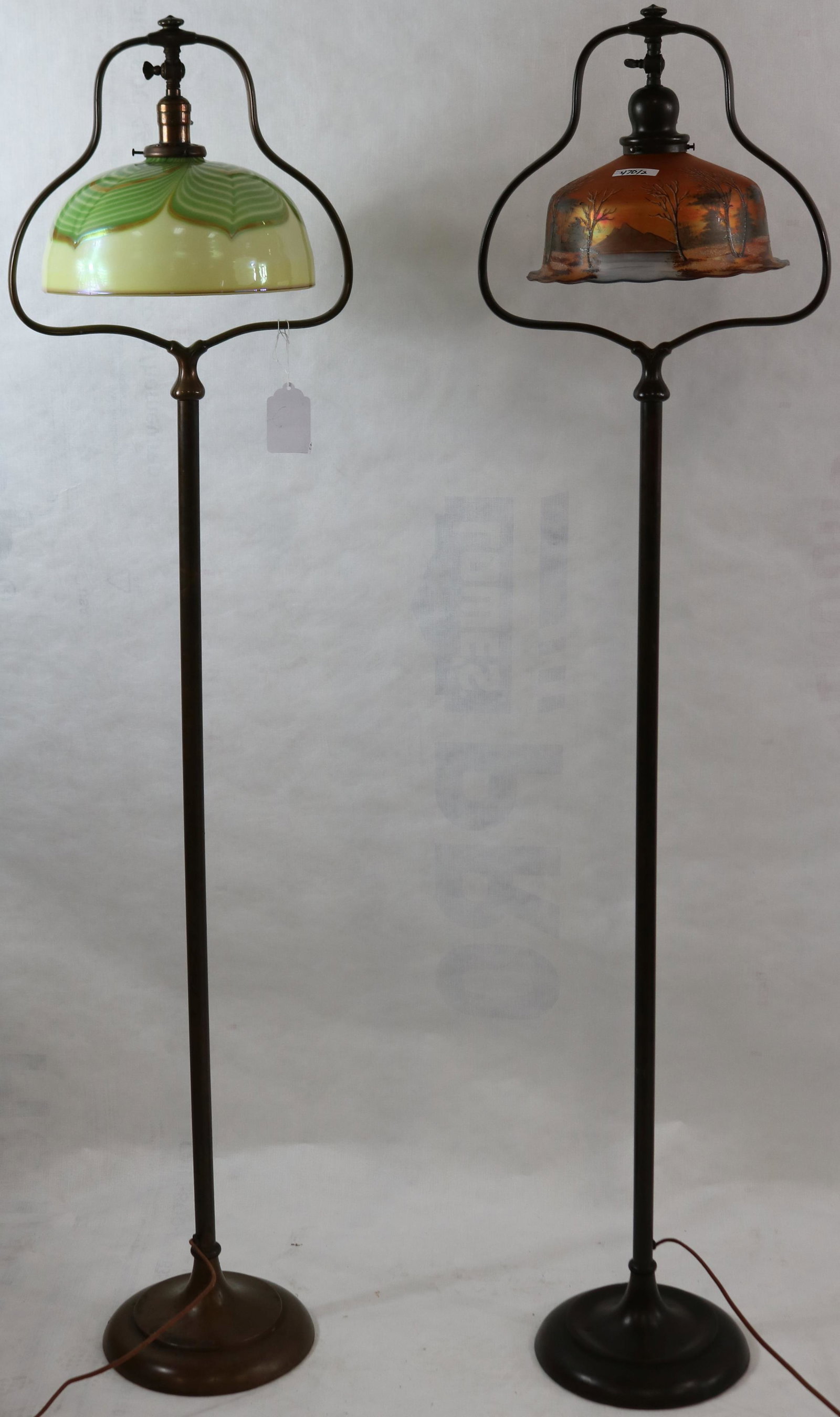 TWO HANDEL STYLE EARLY 20TH CENTURY BRONZE FLOOR: LAMPS. UNSIGNED. HARP TOP. ONE WITH SIGNED LUNDBERG SHADE, PULL THREAD, LARGE CRACK. THE OTHER SHADE IS A VINTAGE SHADE WITH LANDSCAPE PAINTED DESIGN. APPROX. 57 1/2" HIGH, 13 1/2" WIDE.