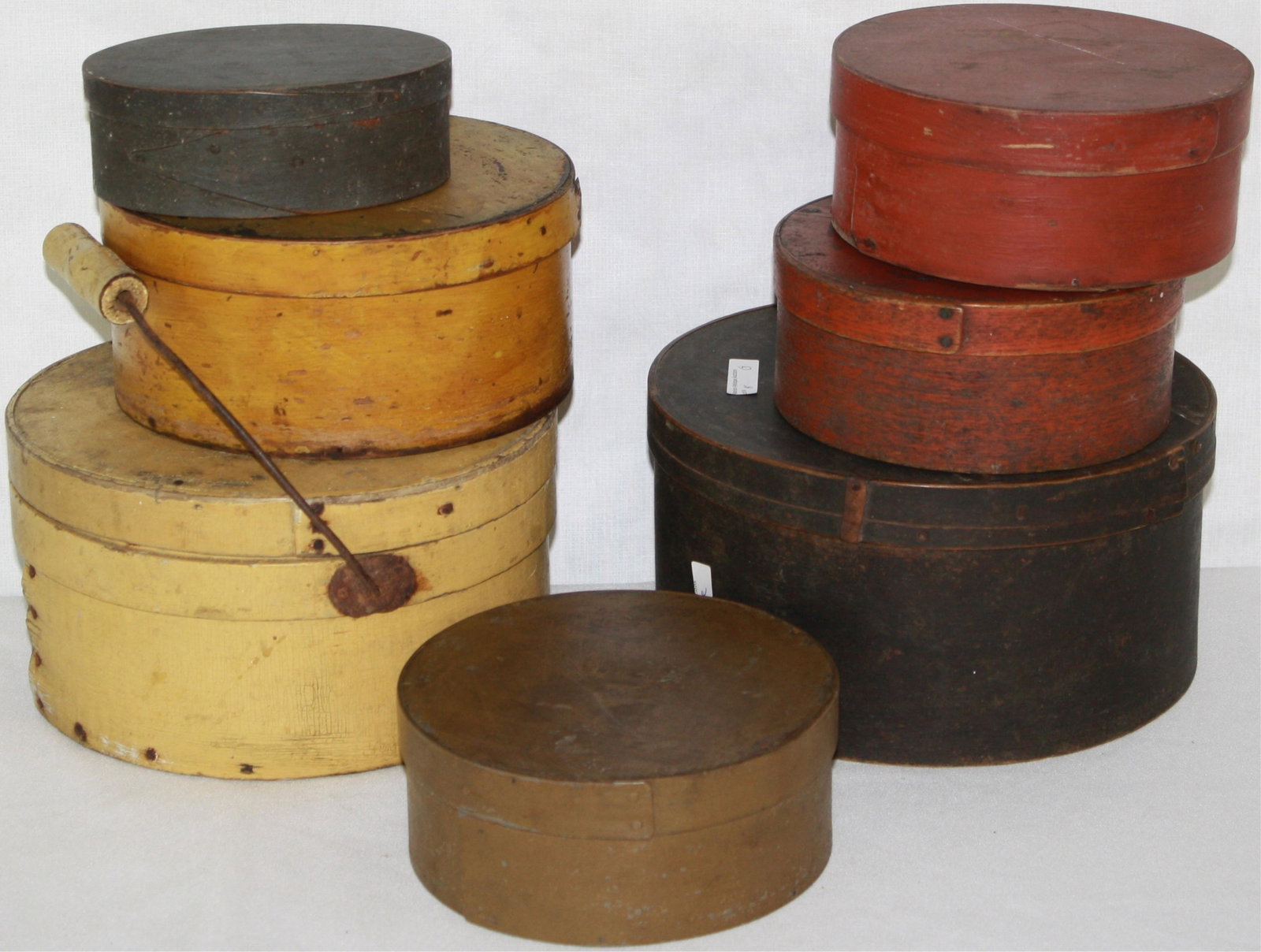 SEVEN 19TH CENTURY PAINTED AMERICAN PANTRY BOXES.: TO INCLUDE: ROUND YELLOW BOX WITH IRON SWING HANDLE, ORIGINAL WORN YELLOW PAINT (9" DIAMETER, 5 1/2" HIGH, SHOWS MINOR BUCKLING TO SEAM), SMALL OVAL BOX WITH ORIGINAL DARK GREEN PAINT (6" LONG, 4 1/2"