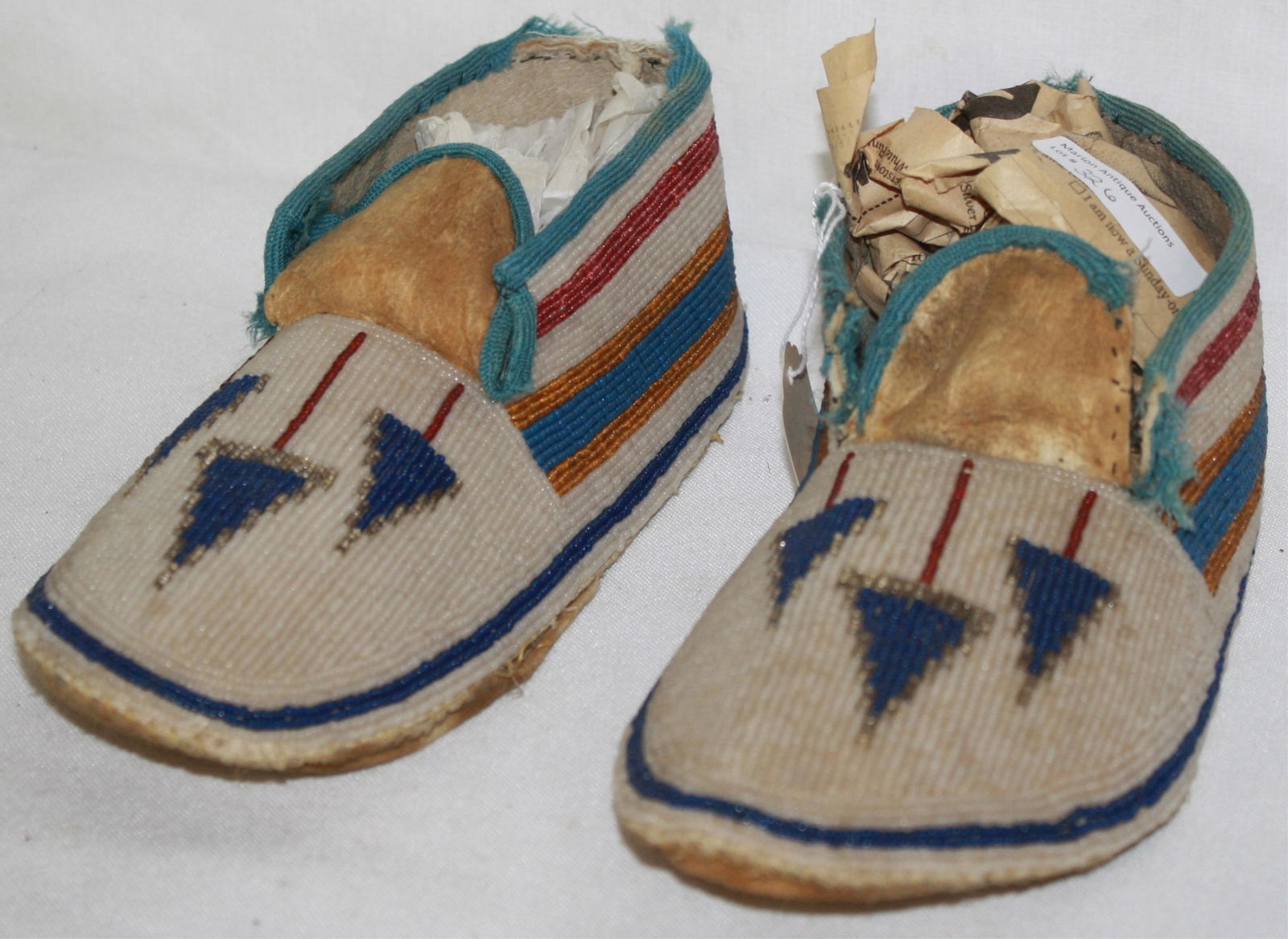 EARLY 20TH CENTURY BEADED PLAINS MOCCASINS, BLUE: ARROW DESIGN ON A WHITE GROUND. 9 1/2" LONG, 3 3/4" WIDE. NATIVE AMERICAN. GOOD CONDITION, SOME LOSS TO WOOL AROUND OPENING.