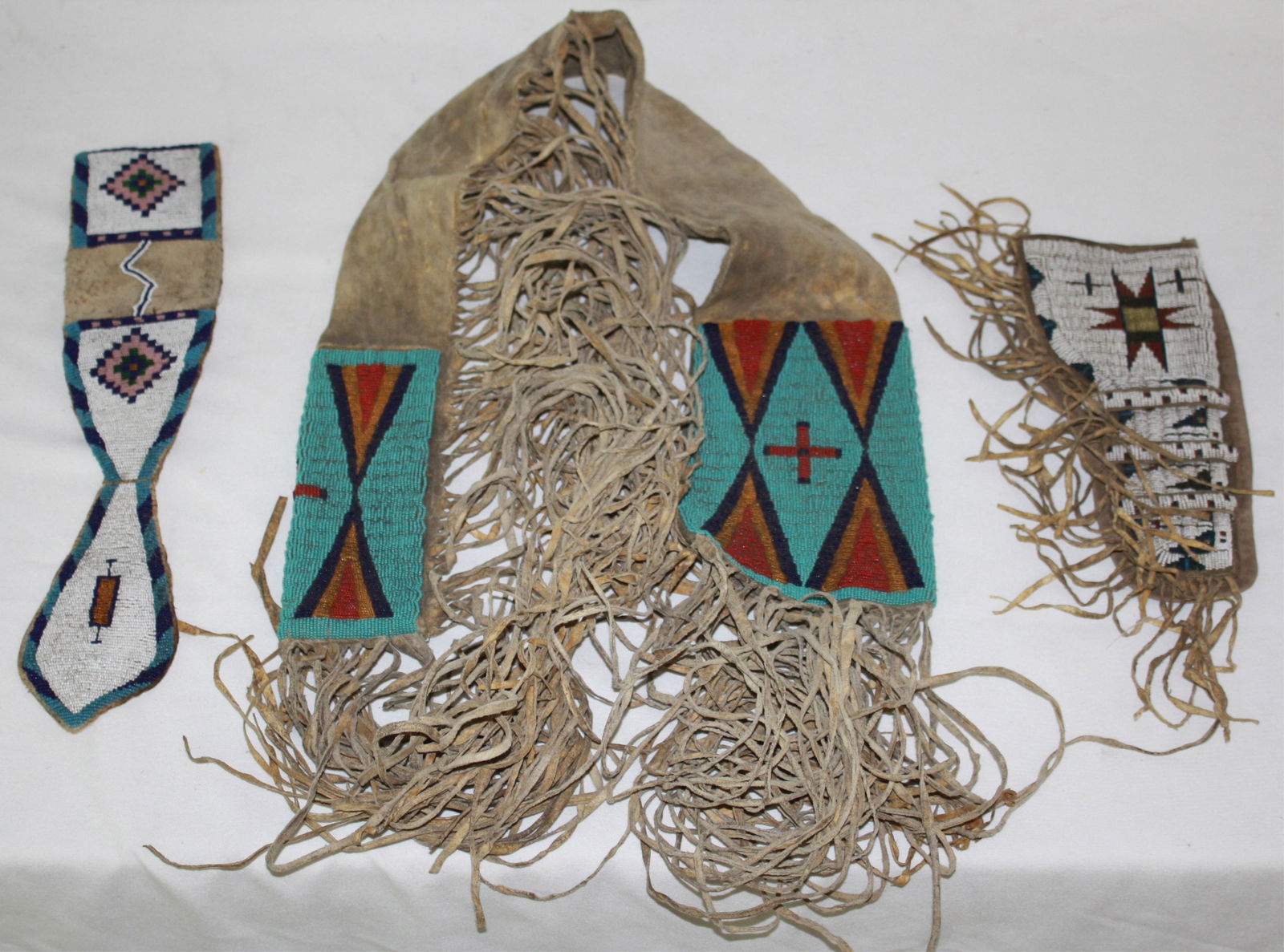 THREE PIECES OF NATIVE AMERICAN BEADWORK ITEMS.: TO INCLUDES: GUN CASE, FRINGED, 46" LONG, GEOMETRIC BEADWORK. HOLSTER, GEOMETRIC DESIGN, 11 1/2" LONG, 5" WIDE. KNIFE CASE, 19" LONG, 4" WIDE. MID-20TH CENTURY.