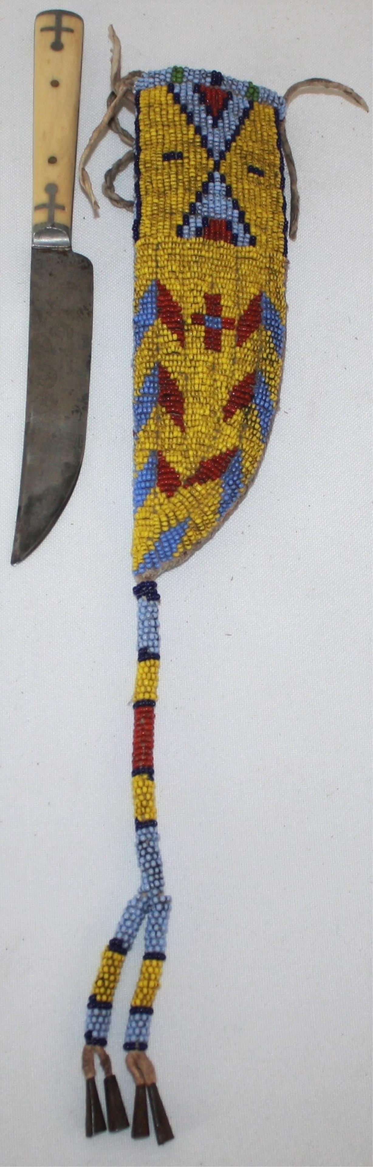 LATE 19TH CENTURY PLAINS BEADED KNIFE SHEATH.: YELLOW, BLUE, RED, AND GREEN BEADWORK. LONG TASSEL WITH TIN CONICAL ENDS. COMES WITH A BONE HANDLED KNIFE. NATIVE AMERICAN. 13 1/2" OVERALL LENGTH, 2" WIDE. OVERALL EXCELLENT CONDITION.