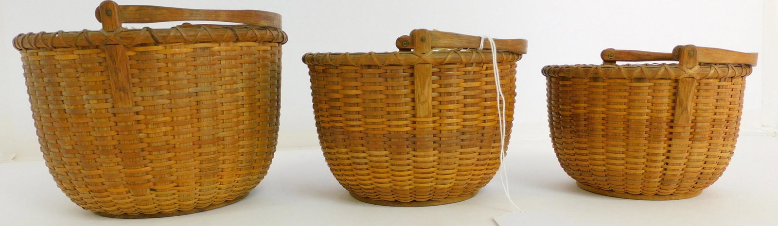 Rowland Folger (1803-1883) nest of three 19th: century Nantucket baskets. Signed on bottom with stencil mark. Hinged wooden swing handle with copper rivets. Wood bottom. Woven with cane and white oak staves, unusually carved. One is 6" in diameter