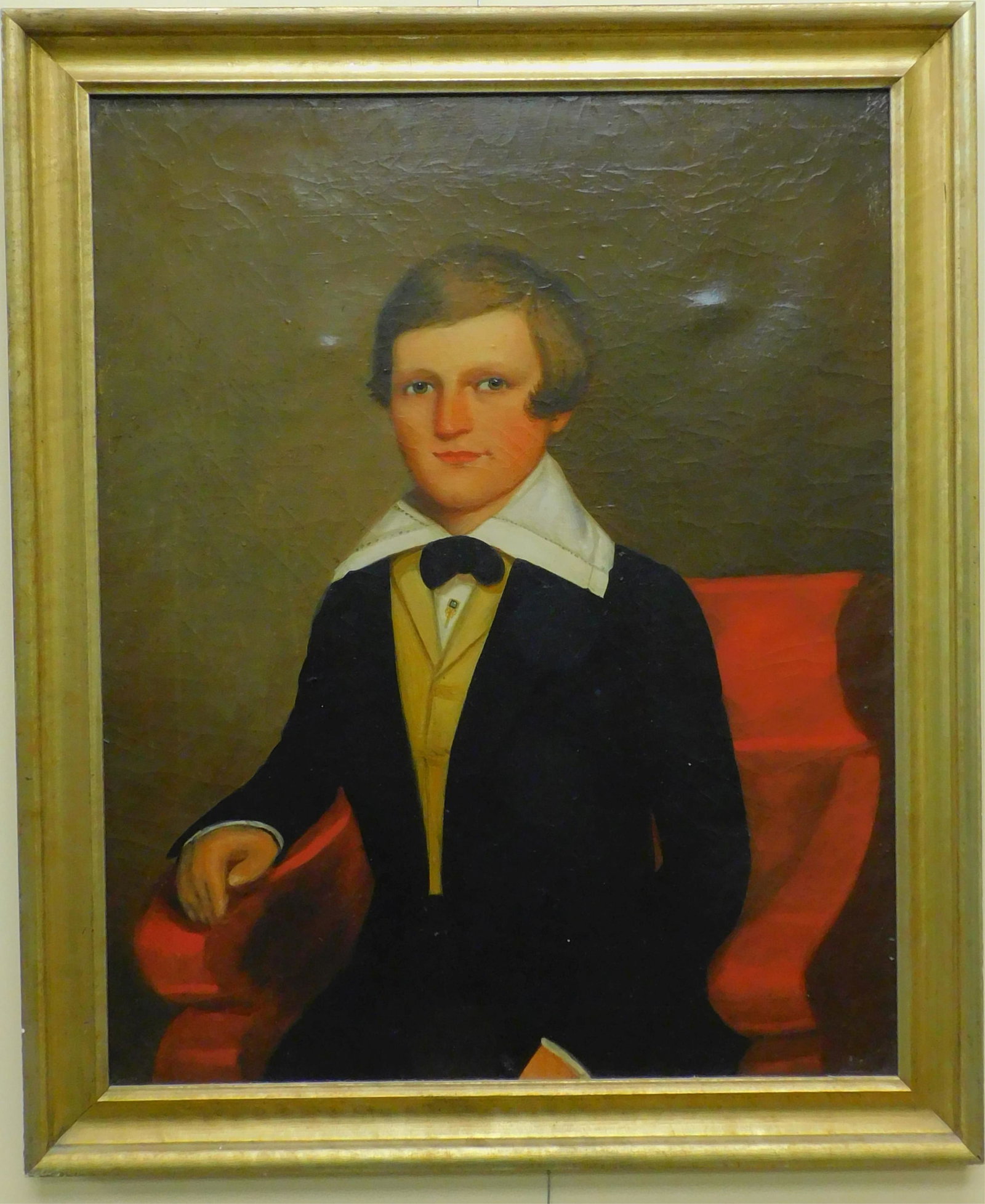 Early 19th century portrait of a young man, oil: painting on canvas, seated in a classical style armchair. Wearing a fine suit and a pale yellow vest. Canvas printed "Nashua" on verso. Sight size 31" x 25", overall with later carved gilded frame 35 