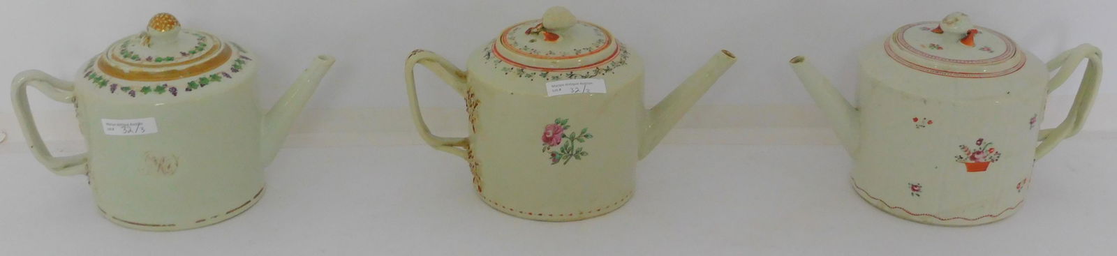 Three Chinese export porcelain teapots with strap: handles, fruit finials, late 18th century. Floral, grape motifs. Approx. 6 1/4" high, 9 3/4" wide. Good overall condition. One handle shows old professional repair.