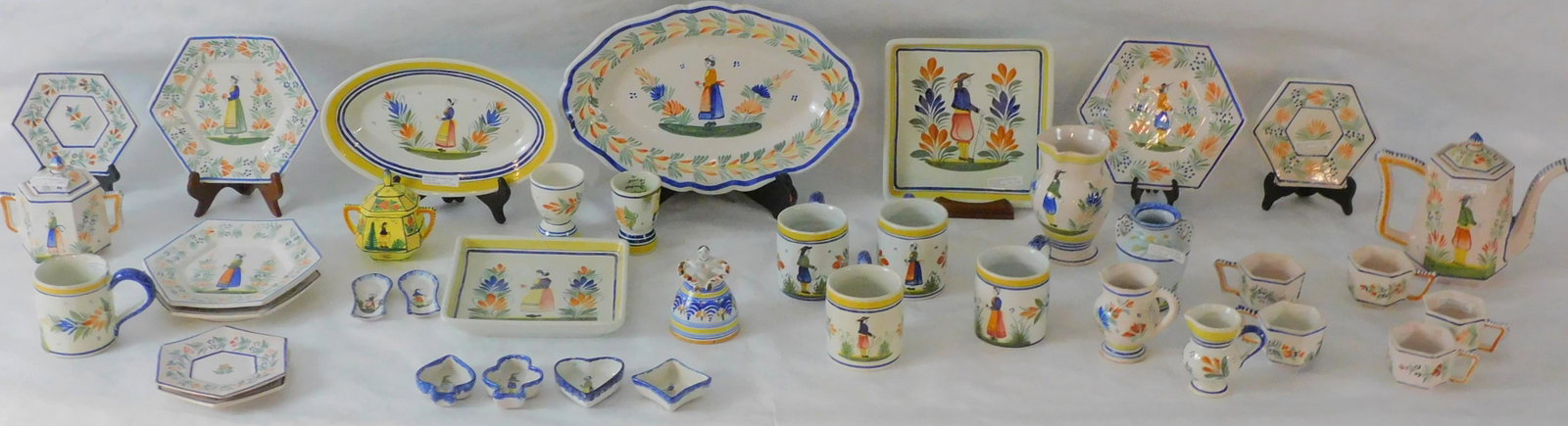 38 pieces of Quimper tableware. To include: 7": teapot, 5 1/2" sugar bowl, four 8 1/4" diameter six sides plates, four 6 1/4" diameter six sided plates, 6" creamer, five 2 1/4" six sided cups (one handle as-is), 4 1/2" covered creamer, 4 1/2" two h