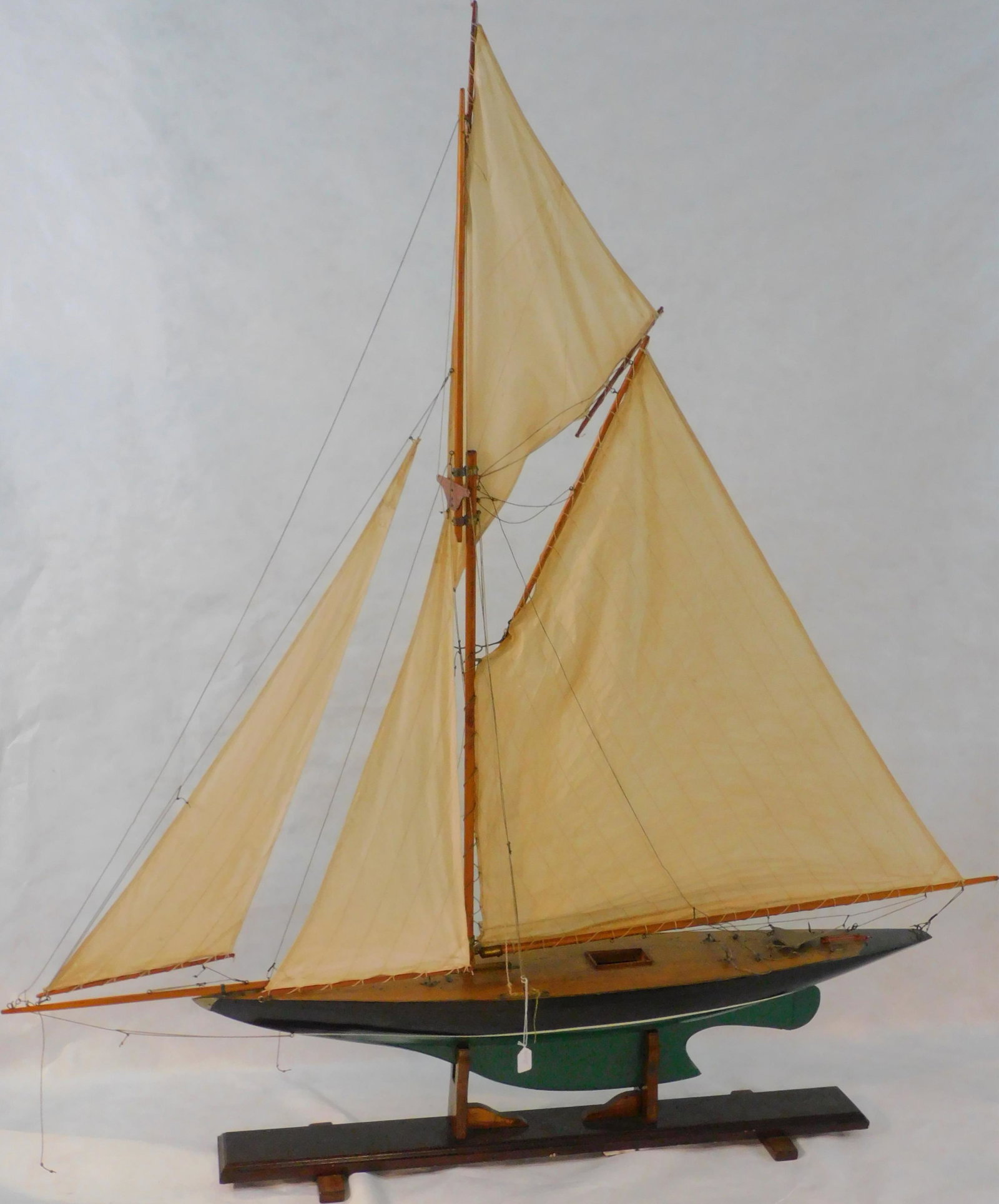20th century pond model of a gaff-rigged yacht. Hull: is painted black above, and green below the waterline. Canvas sails. 73" high, 72" long. Overall good condition, mounted on a custom-made stand.