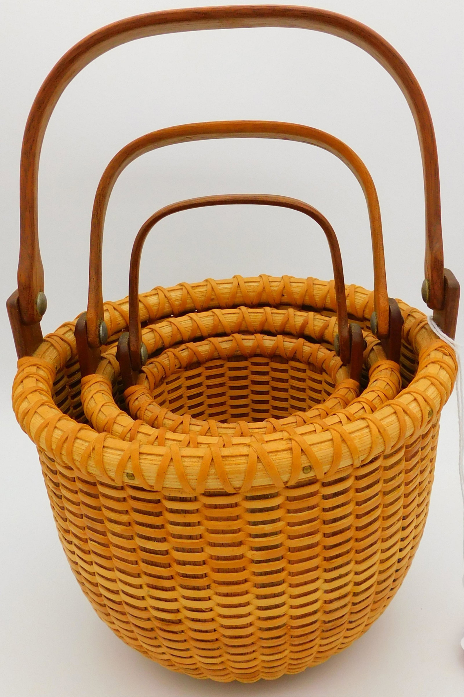 Nest of three round diminutive Nantucket baskets: made by Ainsley D. Rookwood, Cape Cod. Late 20th century Wooden swing handles, signed on bottom ADR. 5 1/4", 7", and 8 1/2" high with handles. Excellent original condition and finish.