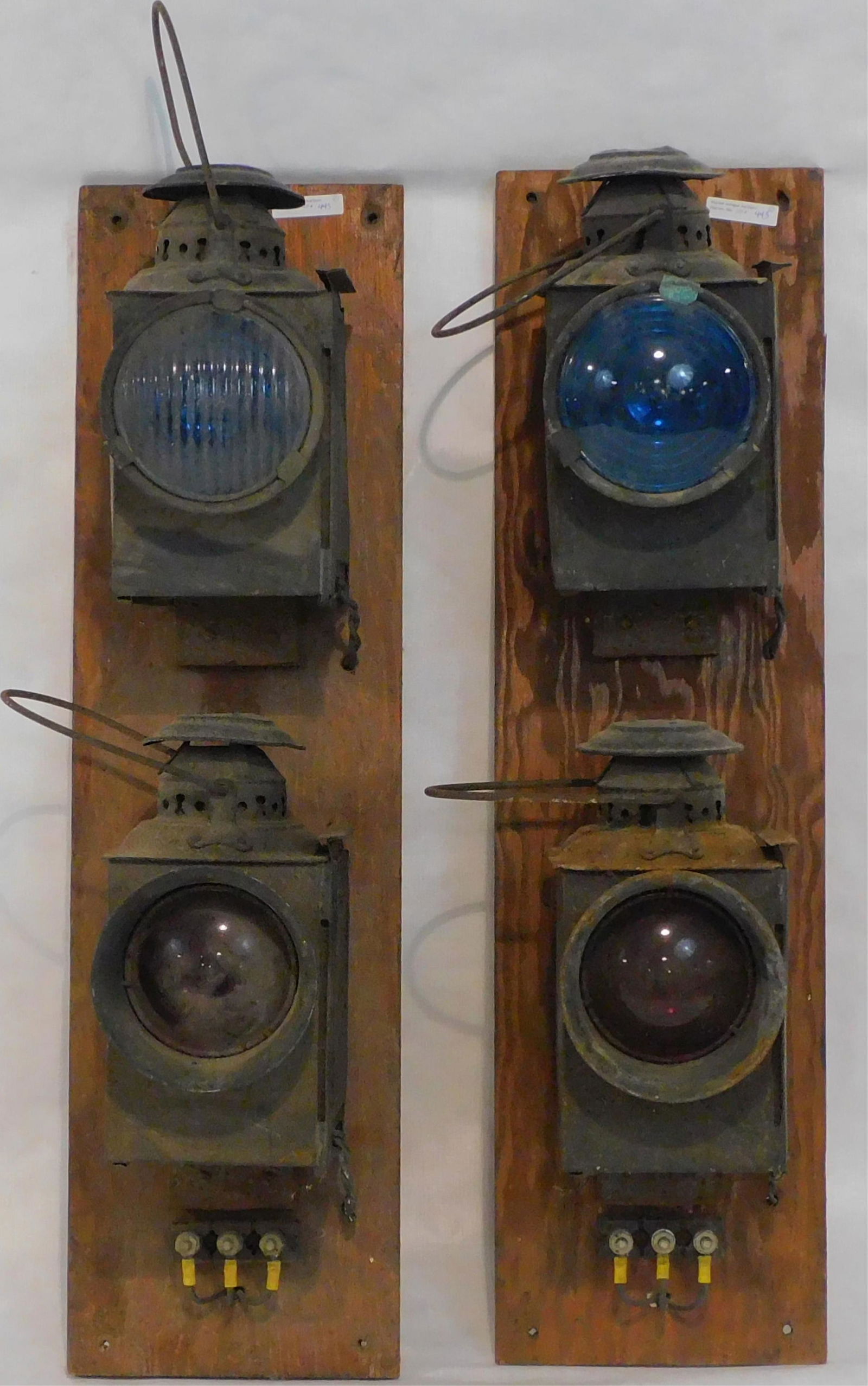 Four mounted railroad signal lanterns. All are: 11" high, with the handle adding another 4". Two have blue lenses, and two have red lenses. Fair condition. One has heavy rust, and the others show light rust and corrosion. On wooden mount.